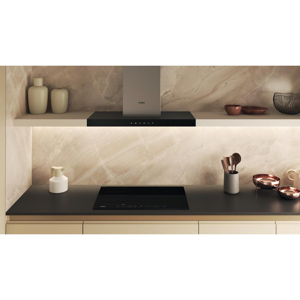 Escena de cocina con placa de cocina negra, campana extractora y objetos de estante. Tonos neutros.