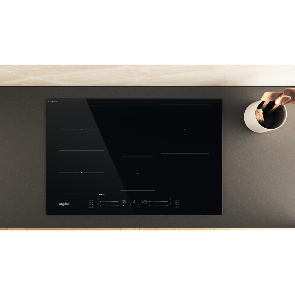 Encimera de vidrio negro sobre encimera gris. Un recipiente blanco con cucharas de madera visible en el fondo.