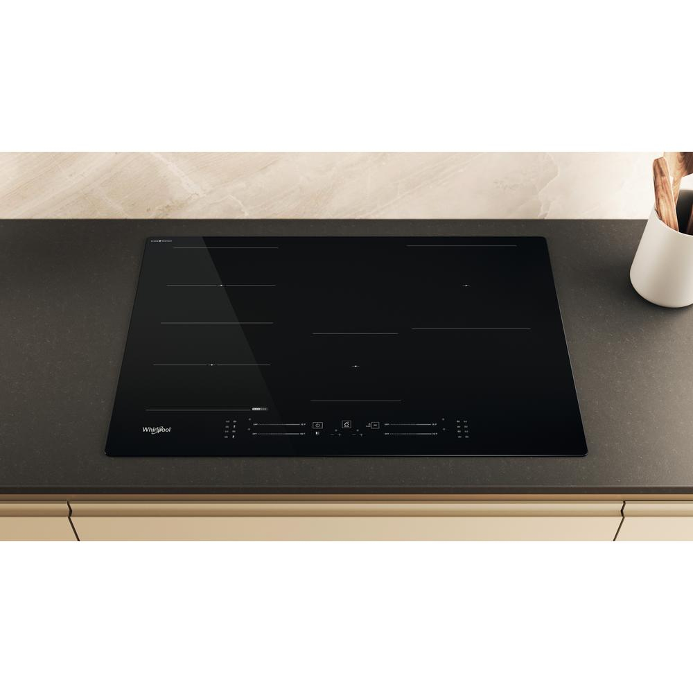 Una placa de inducción negra con cinco quemadores y controles táctiles sobre una encimera beige.