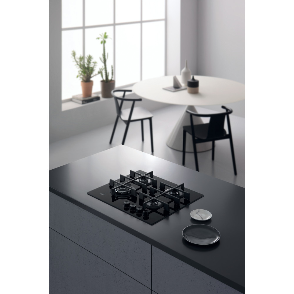 Escena de cocina con encimera de gas negra sobre encimera gris. Mesa blanca y sillas en el fondo.