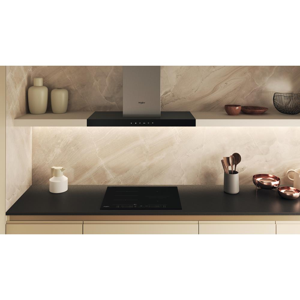 Cucina moderna con piano cottura nero, piano di lavoro in marmo bianco e oggetti decorativi.