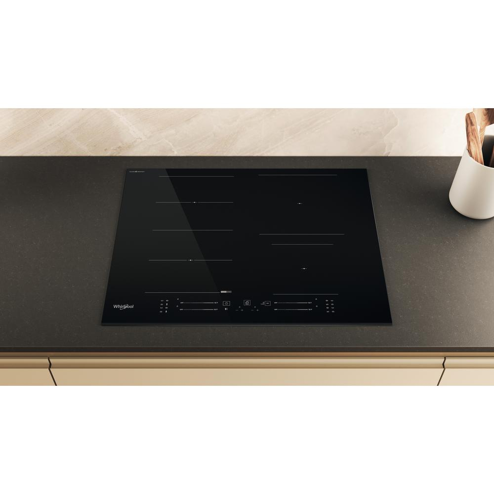 Piano cottura a induzione nero su piano grigio. Sfondo bianco, marchio Whirlpool.