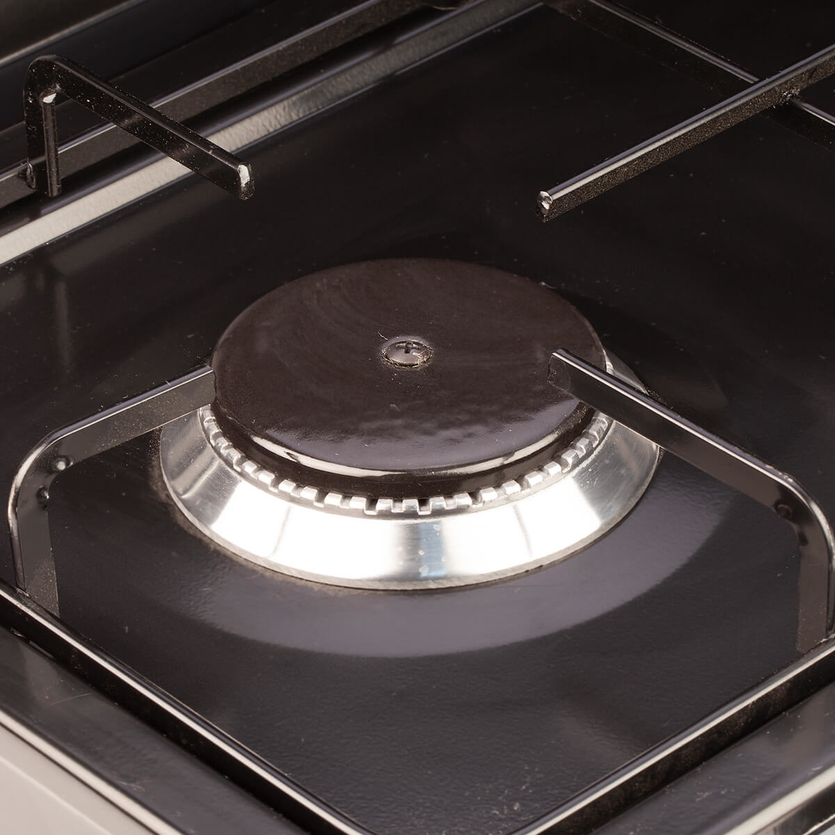 Zbliżenie na czarny palnik kuchenki gazowej z metalową kratką.