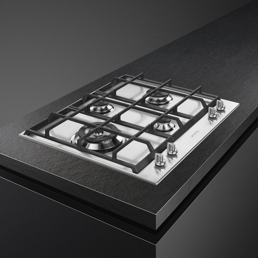 Placa de gas Smeg en encimera oscura. Cuatro quemadores y mandos plateados. Acero inox.