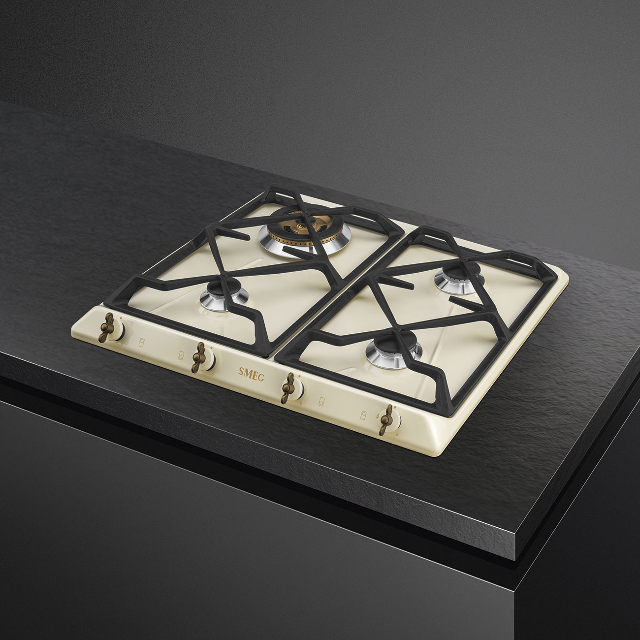 Kremowa płyta gazowa Smeg z czarnymi rusztami i mosiężnymi pokrętłami na ciemnym blacie.