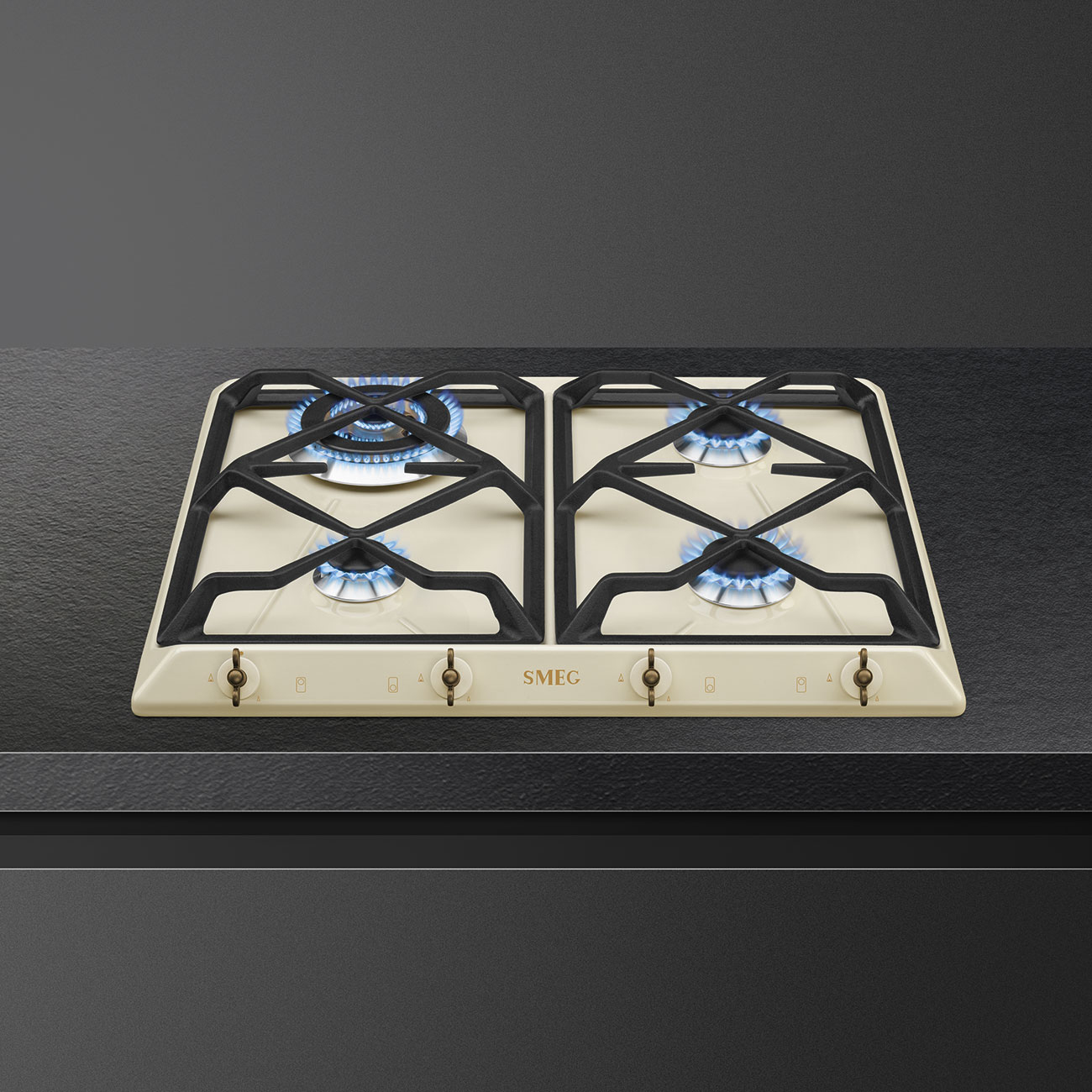 Kuchenka gazowa z czterema palnikami zapalonymi niebieskimi płomieniami i kremową powierzchnią.
