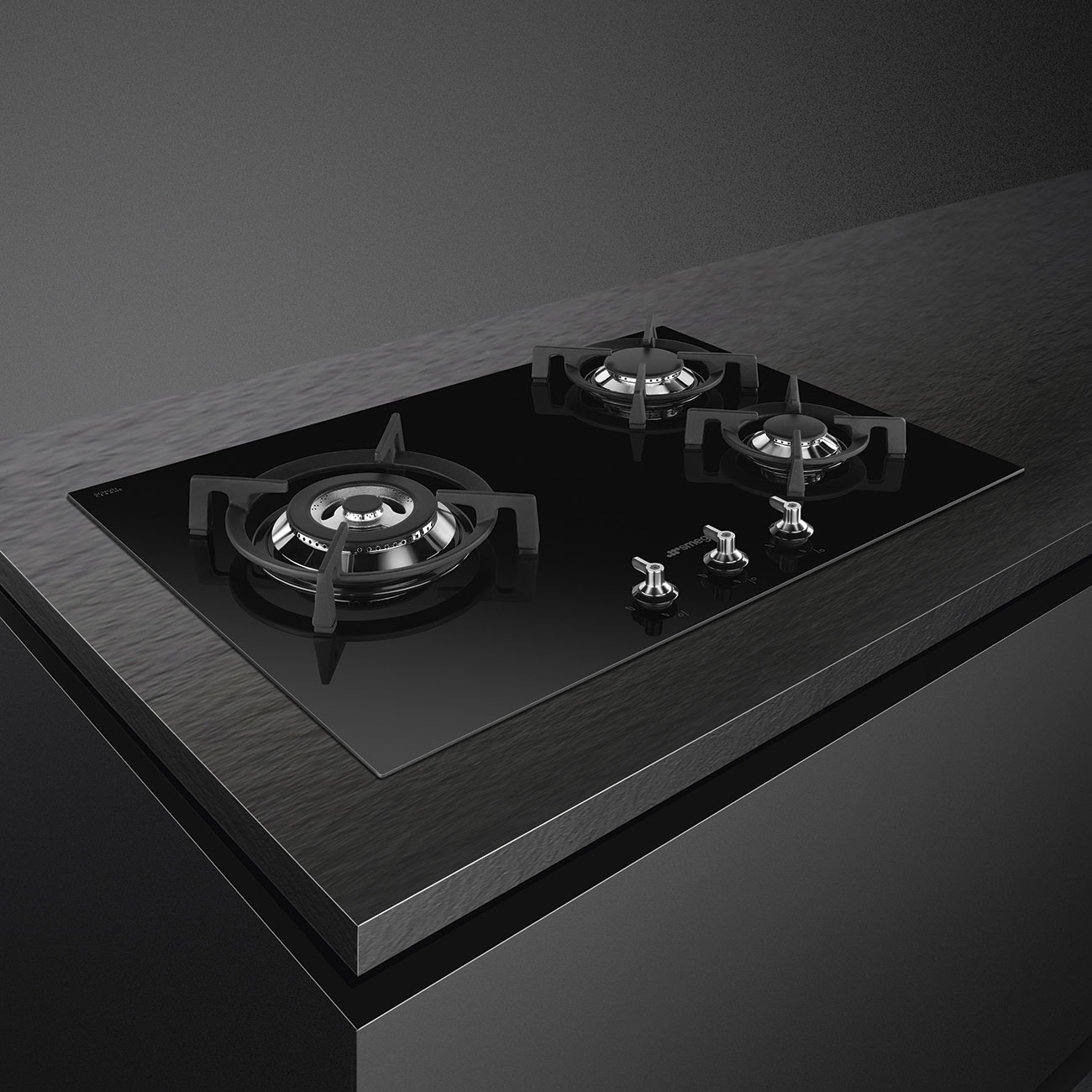 Una placa de cocina negra con tres quemadores, integrada en una encimera oscura.