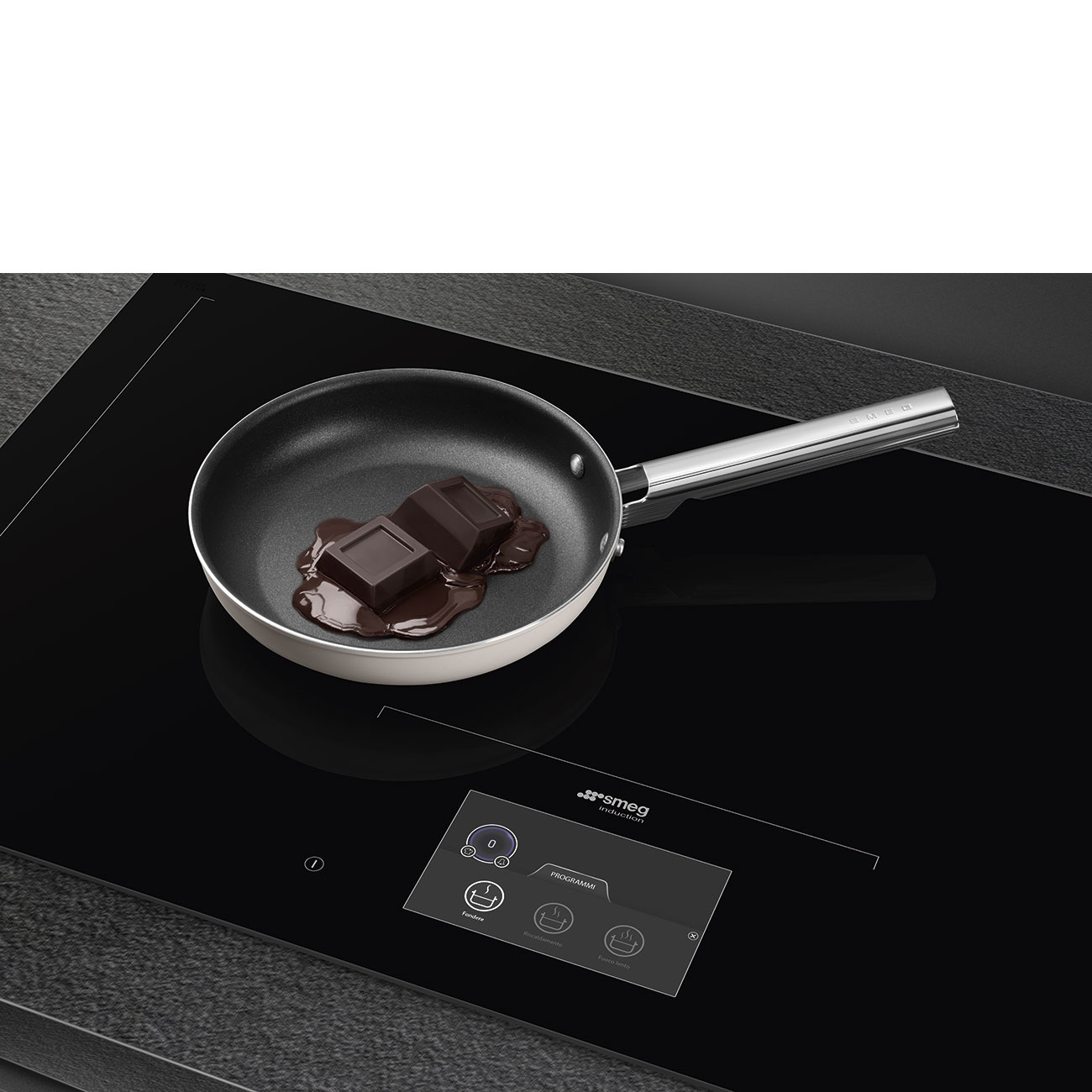 Una piccola padella con cioccolato fuso su un piano cottura nero. Visibile un pannello di controllo.