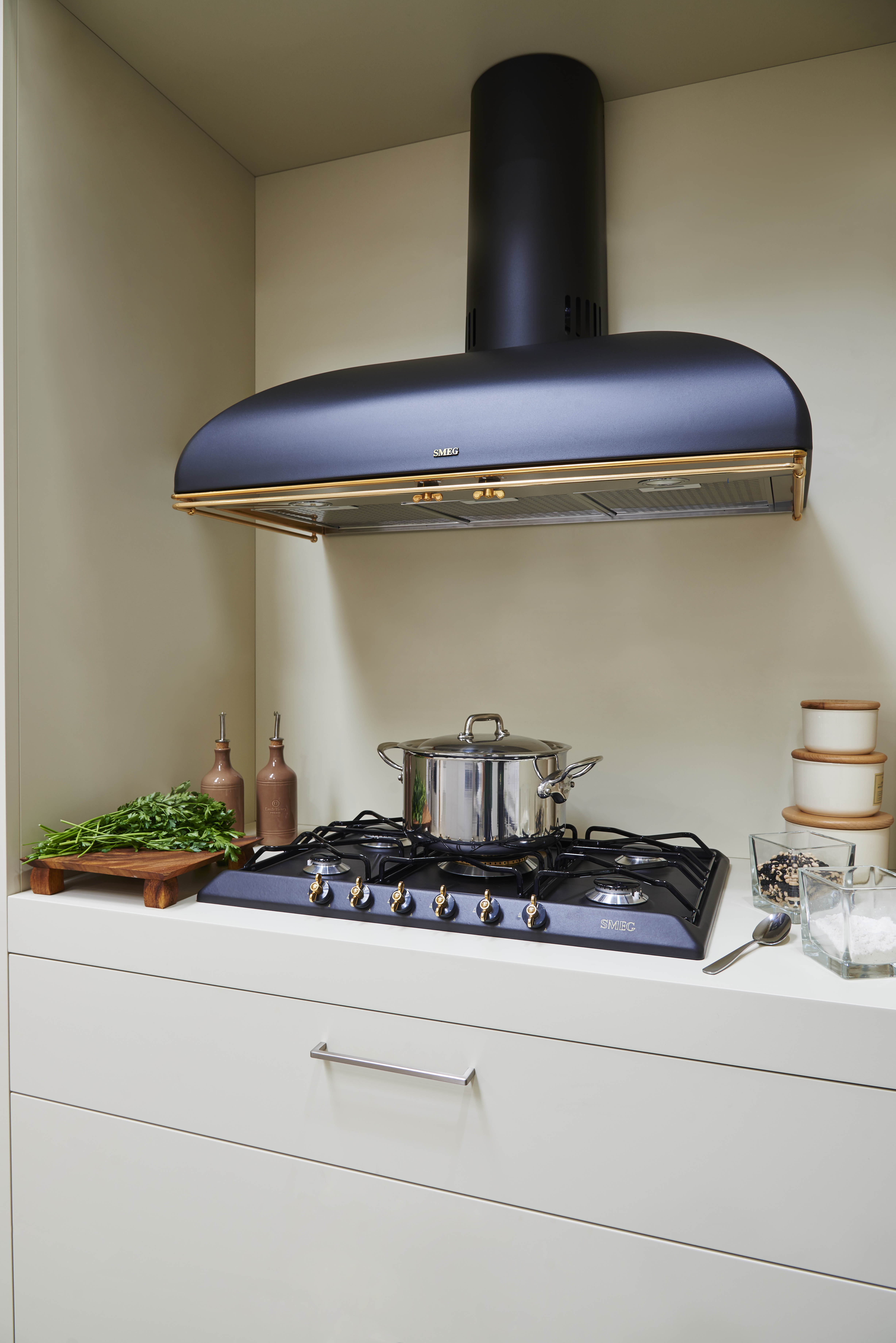 Wnętrze kuchni z kuchenką, okapem i różnymi przedmiotami kuchennymi.