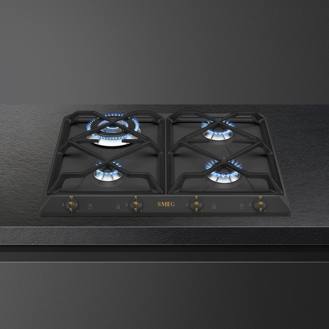 Czarna płyta grzewcza z czterema palnikami. Marka to Smeg. Tło jest ciemnoszare.