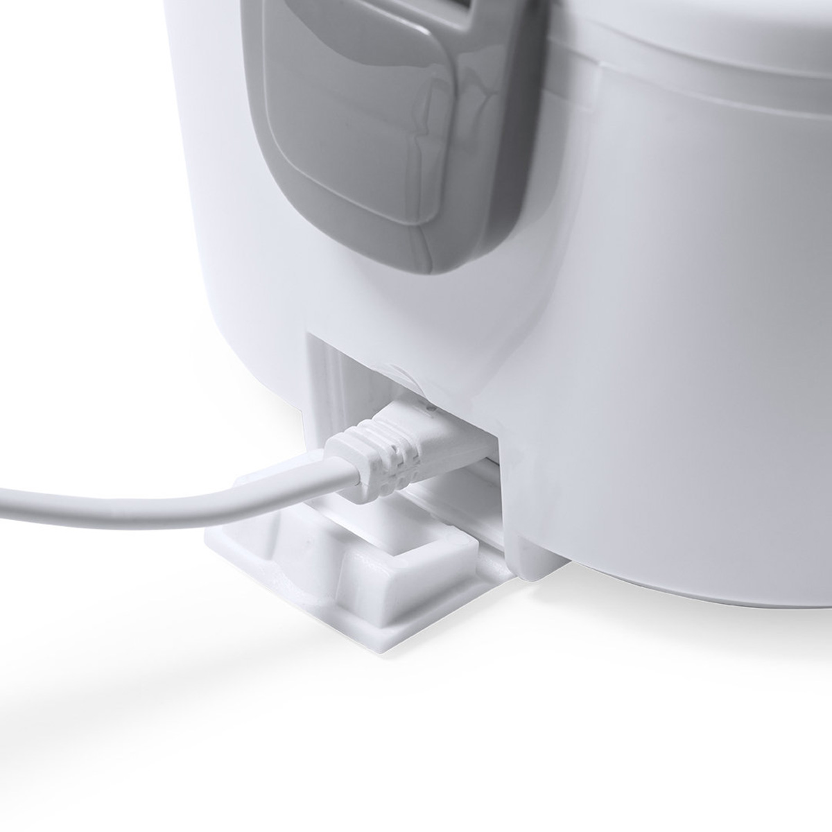 Primer plano de una fiambrera blanca con un cable de carga blanco enchufado. Fondo blanco.