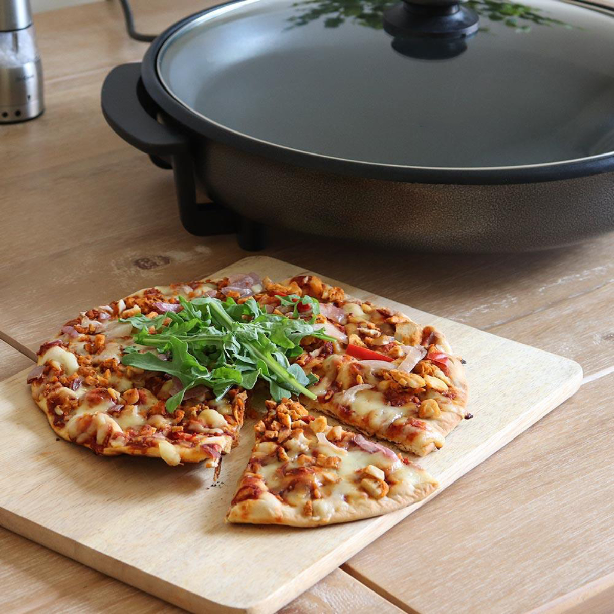 Pizza cortada en una tabla de madera, plancha en el fondo. Mesa de madera.
