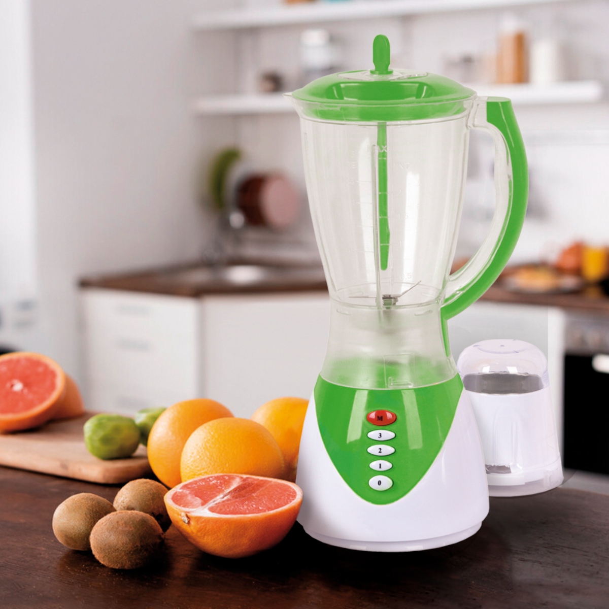 Una licuadora verde y blanca con frutas: pomelo, naranjas, kiwi y limas sobre una mesa.