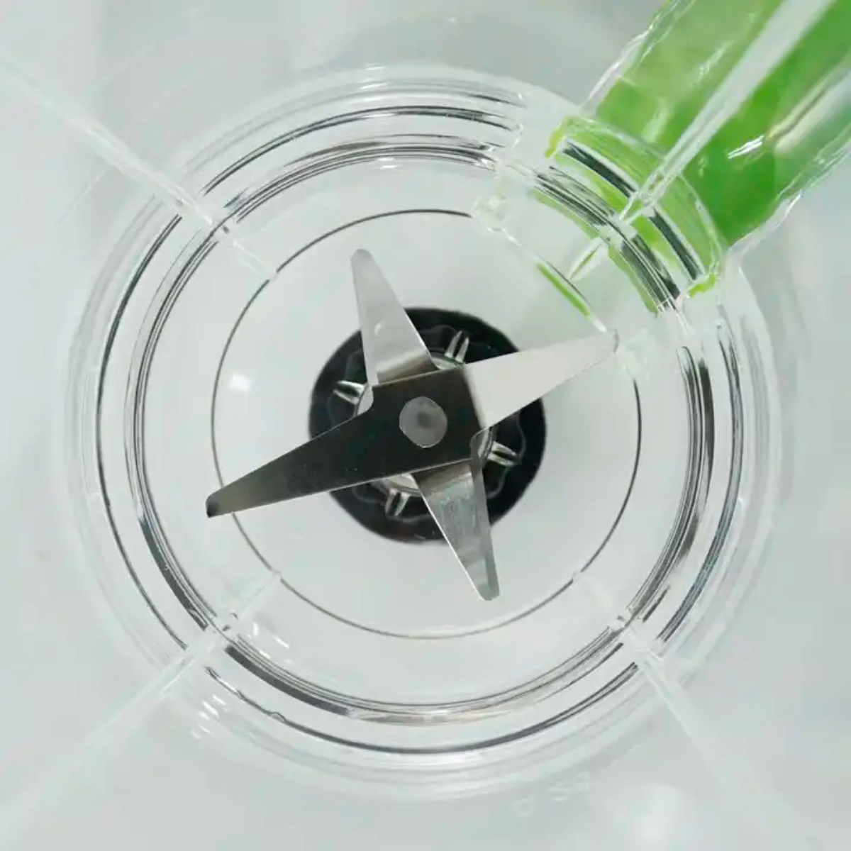 Toma cenital de las cuchillas de la licuadora, con líquido verde vertiéndose.