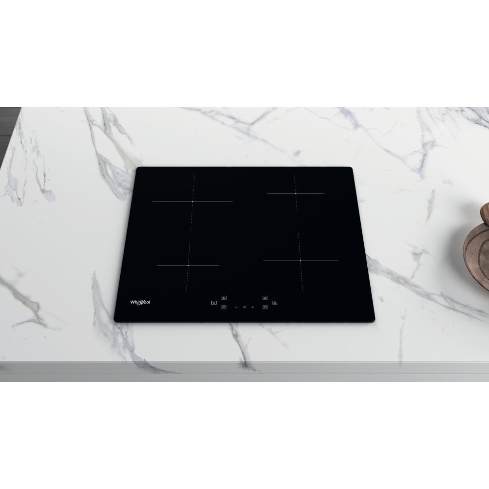 Una placa de cocina negra con cuatro círculos negros, sobre una encimera de mármol blanco.
