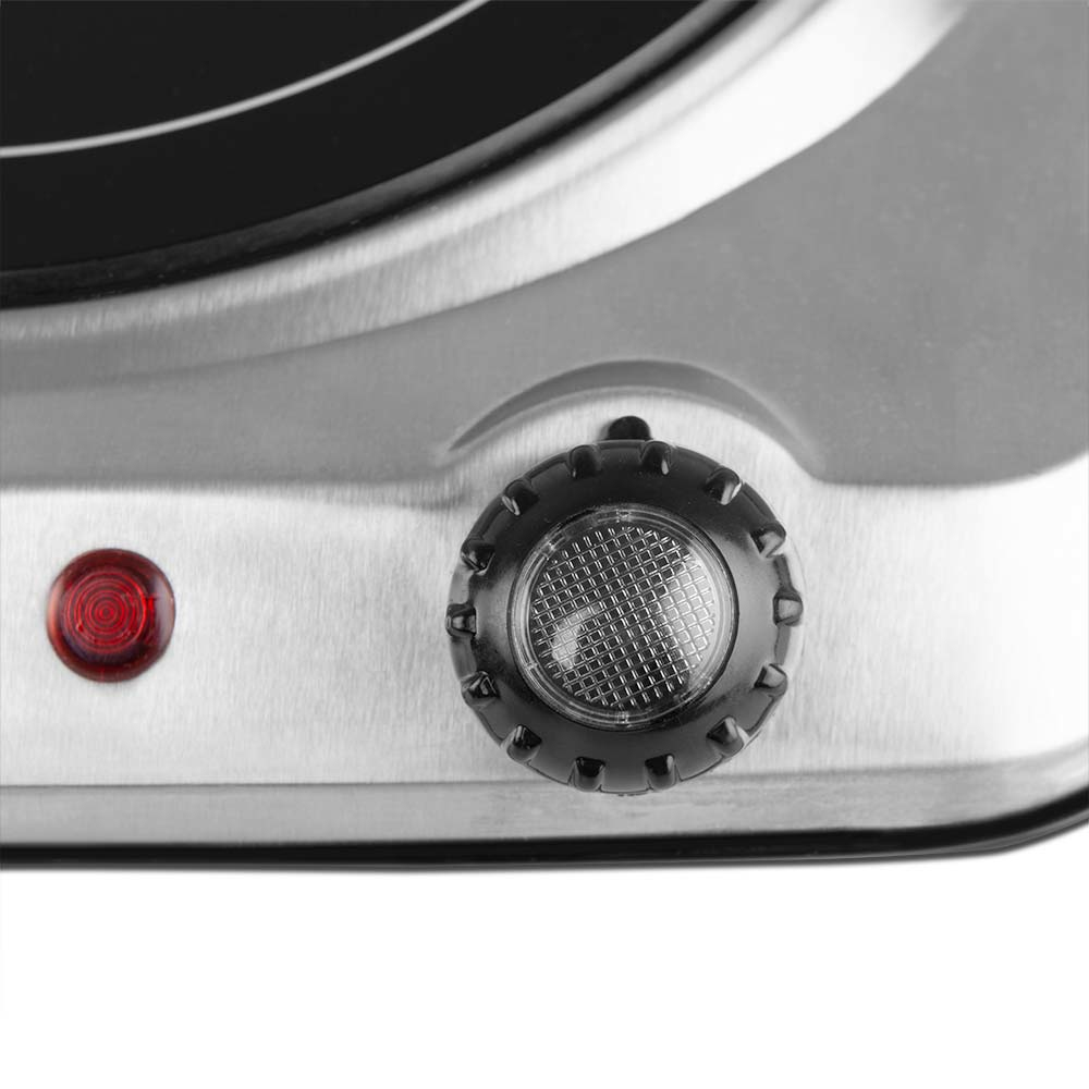 Zbliżenie czarnego pokrętła z czerwoną lampką na srebrnej, elektrycznej płycie grzejnej.