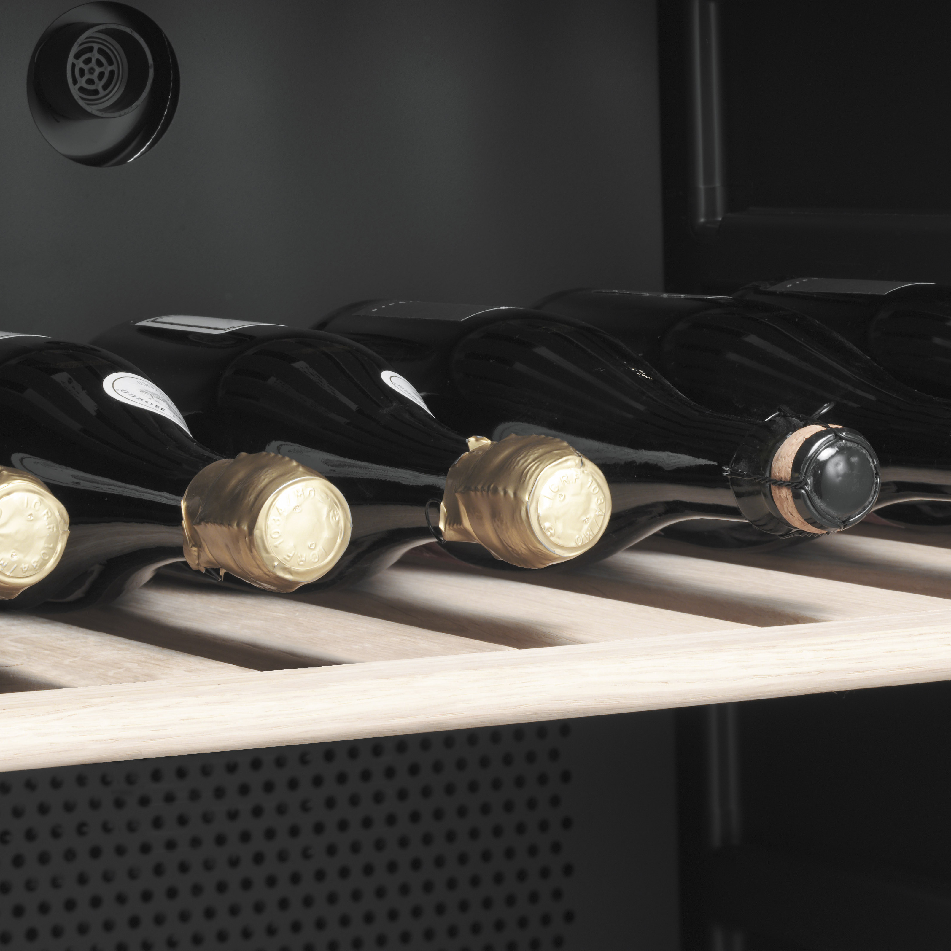 Botellas de vino dispuestas en estantes de madera. Tapones dorados visibles. Fondo oscuro.