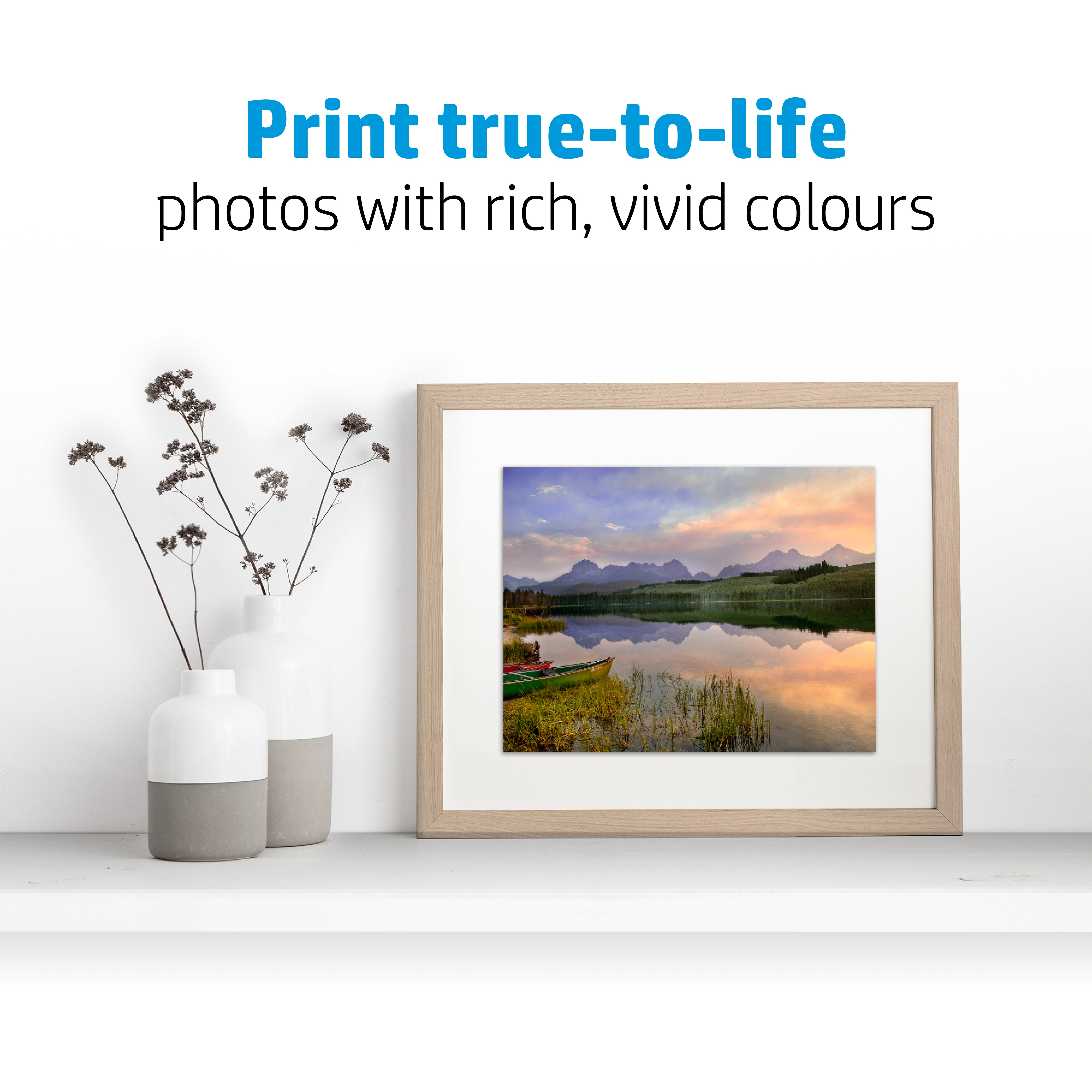 Oprawione zdjęcie jeziora z górami na białej półce, z wazonami.