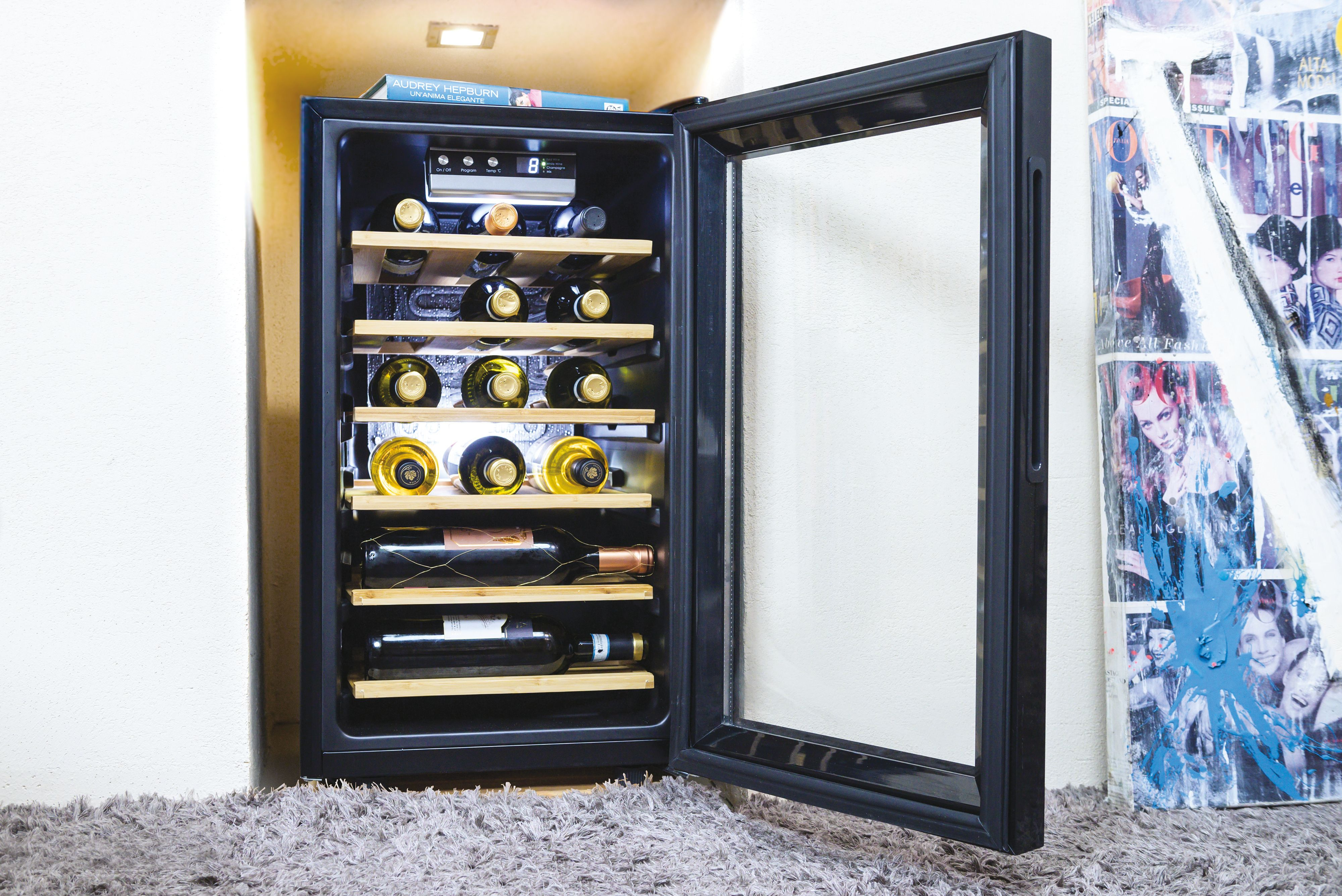 Cantinetta con porta aperta, piena di bottiglie di vino. Tappeto grigio e muro bianco sullo sfondo.