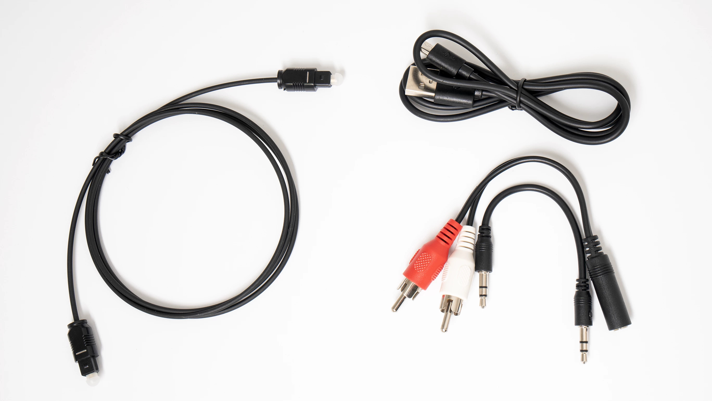 Varios cables negros y cables de audio con enchufes rojos, blancos sobre una superficie blanca. Cables USB, RCA y jack.