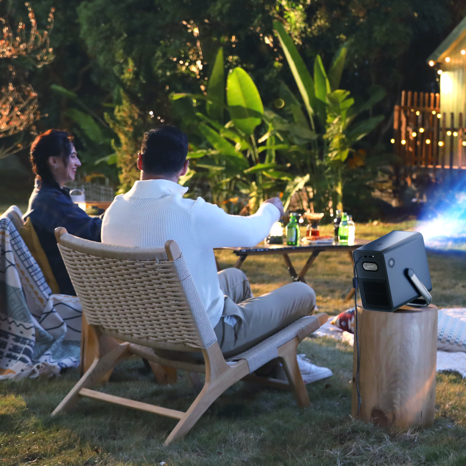 Dwie osoby oglądają film wyświetlany na zewnątrz. Projektor stoi na drewnianym stojaku.