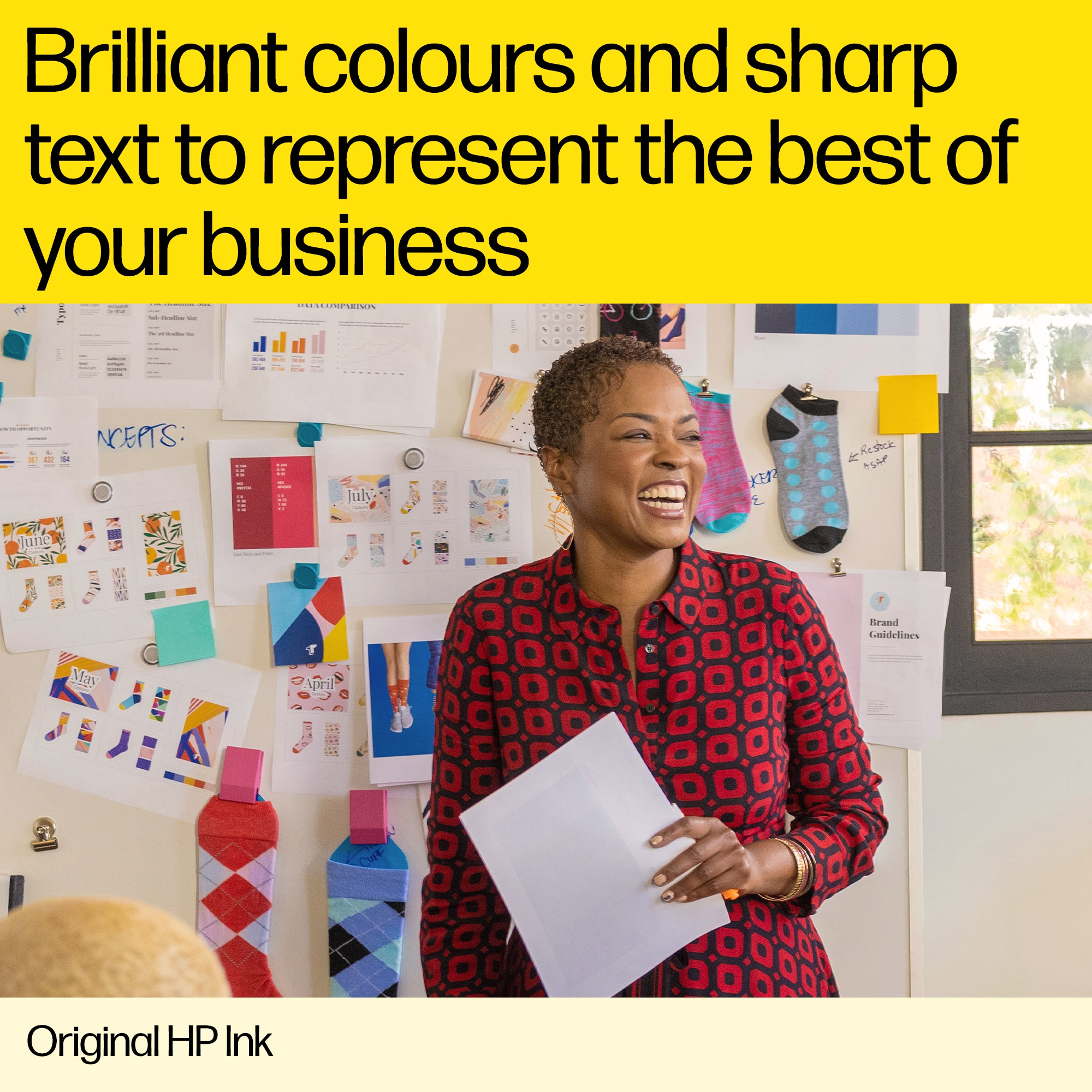 Kobieta trzymająca białą kartkę, uśmiechnięta. Za nią ściana z papierami, skarpetkami i napisem 'Brand Guidelines'.