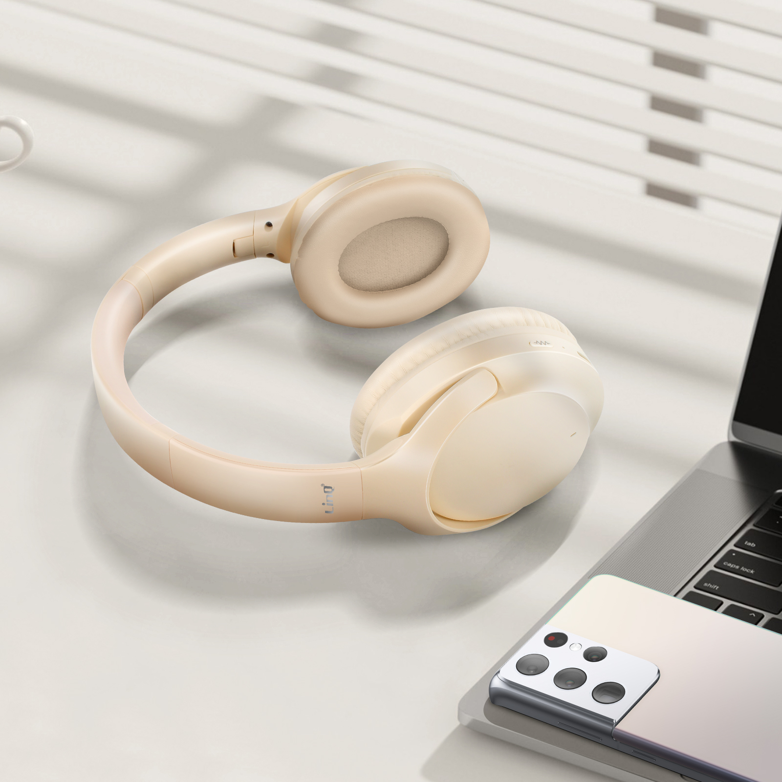 Casque beige sur surface blanche, un ordinateur portable et un téléphone sont visibles en arrière-plan.