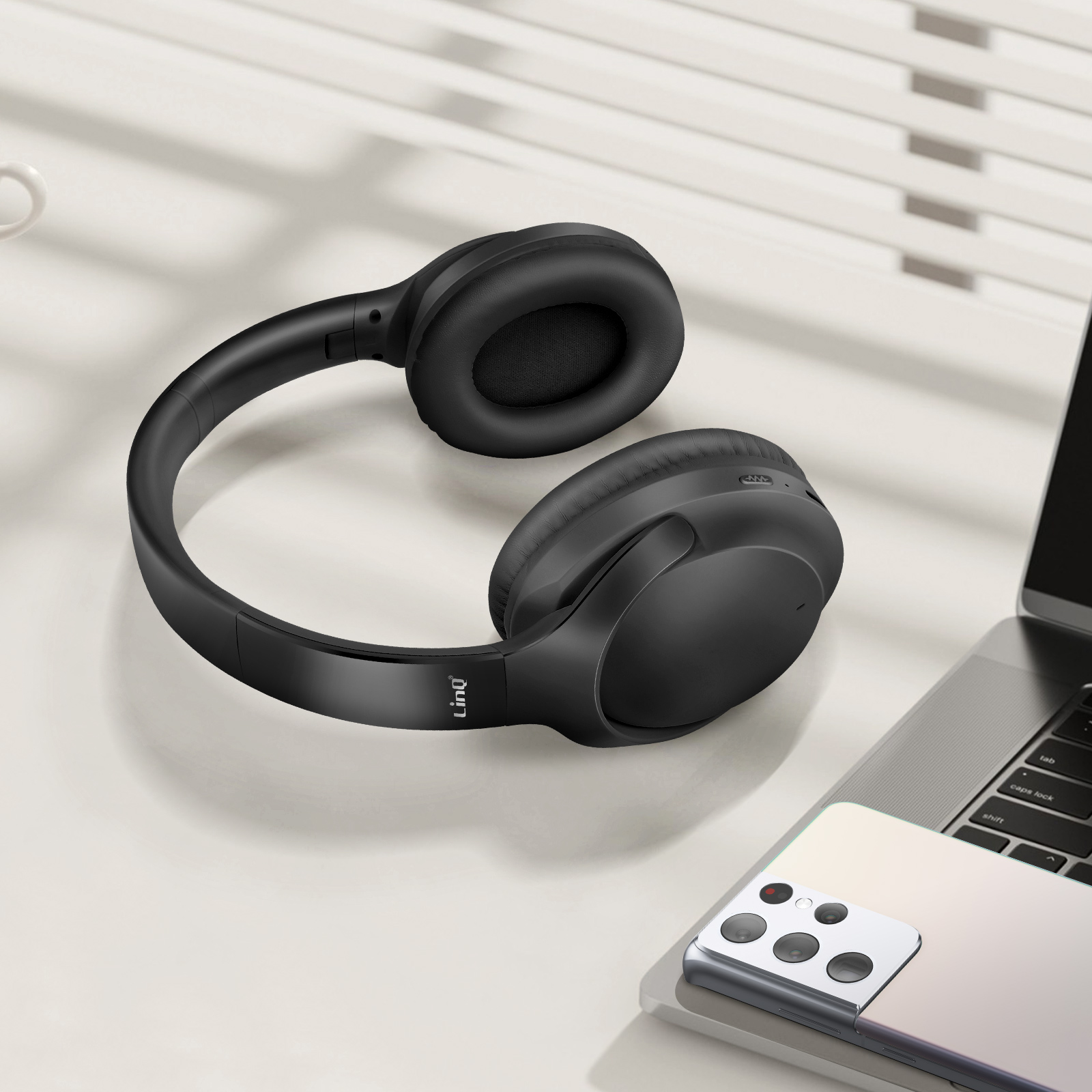 Casque noir sur surface blanche, un ordinateur portable et un téléphone sont visibles en arrière-plan.