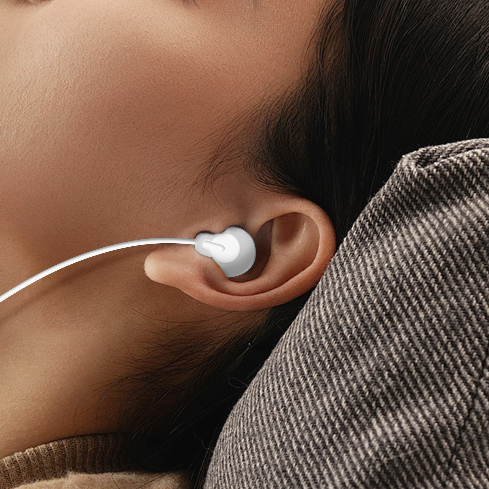 Orecchio di una persona con un auricolare bianco inserito. Tessuto grigio sullo sfondo.