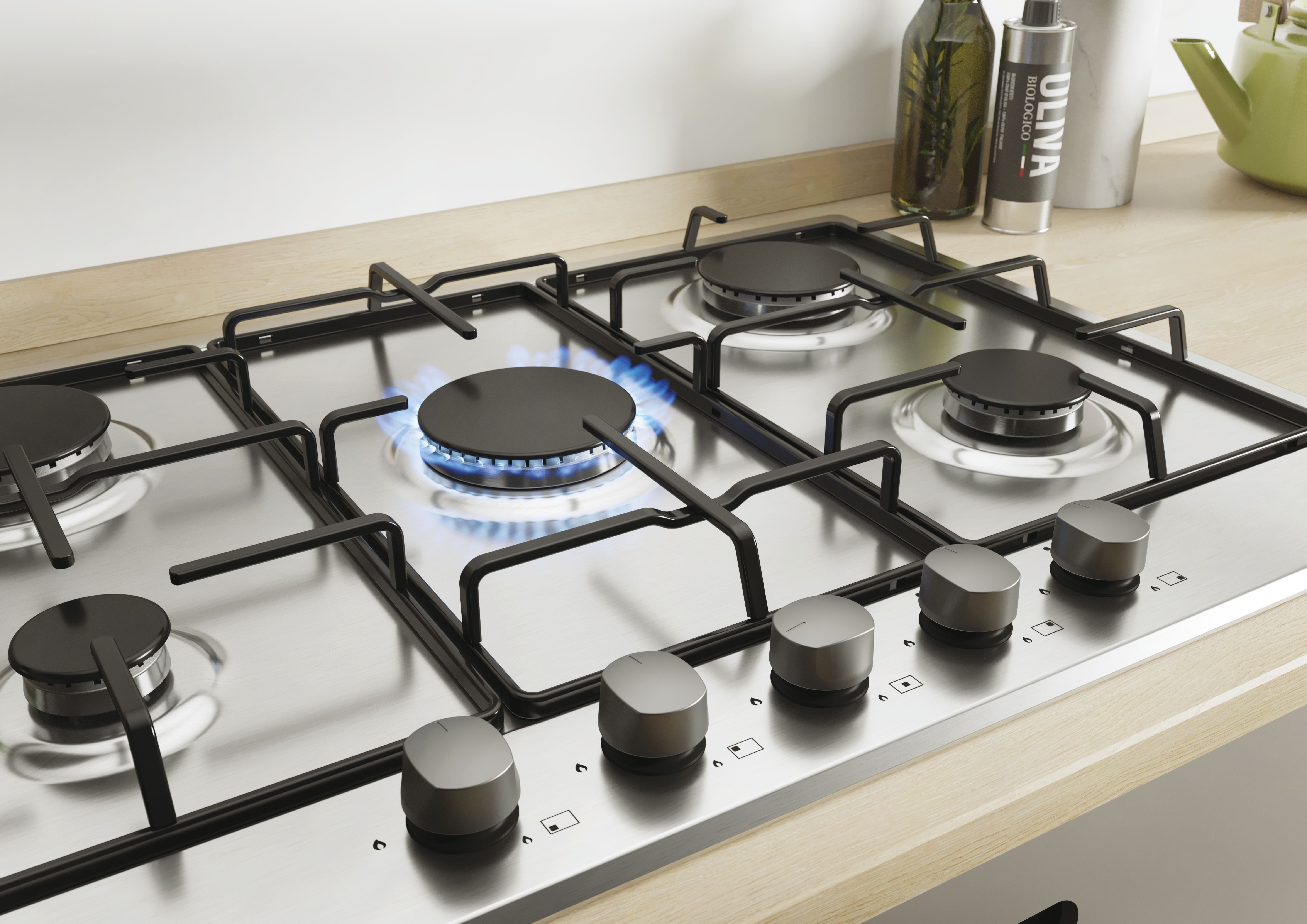 Płyta gazowa z pięcioma palnikami. Jeden palnik płonie niebieskim płomieniem. Pokrętła z przodu.