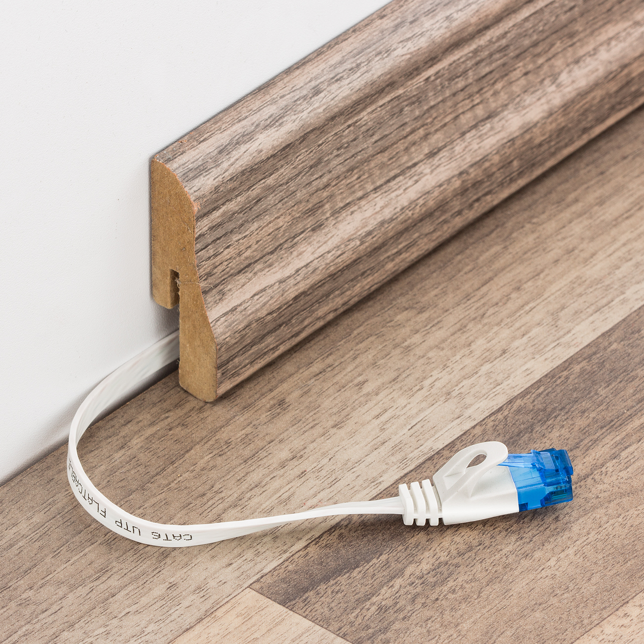 Weißes Ethernet-Kabel kommt aus der Wand, neben Holzverkleidung, mit blauem Stecker auf dem Boden.