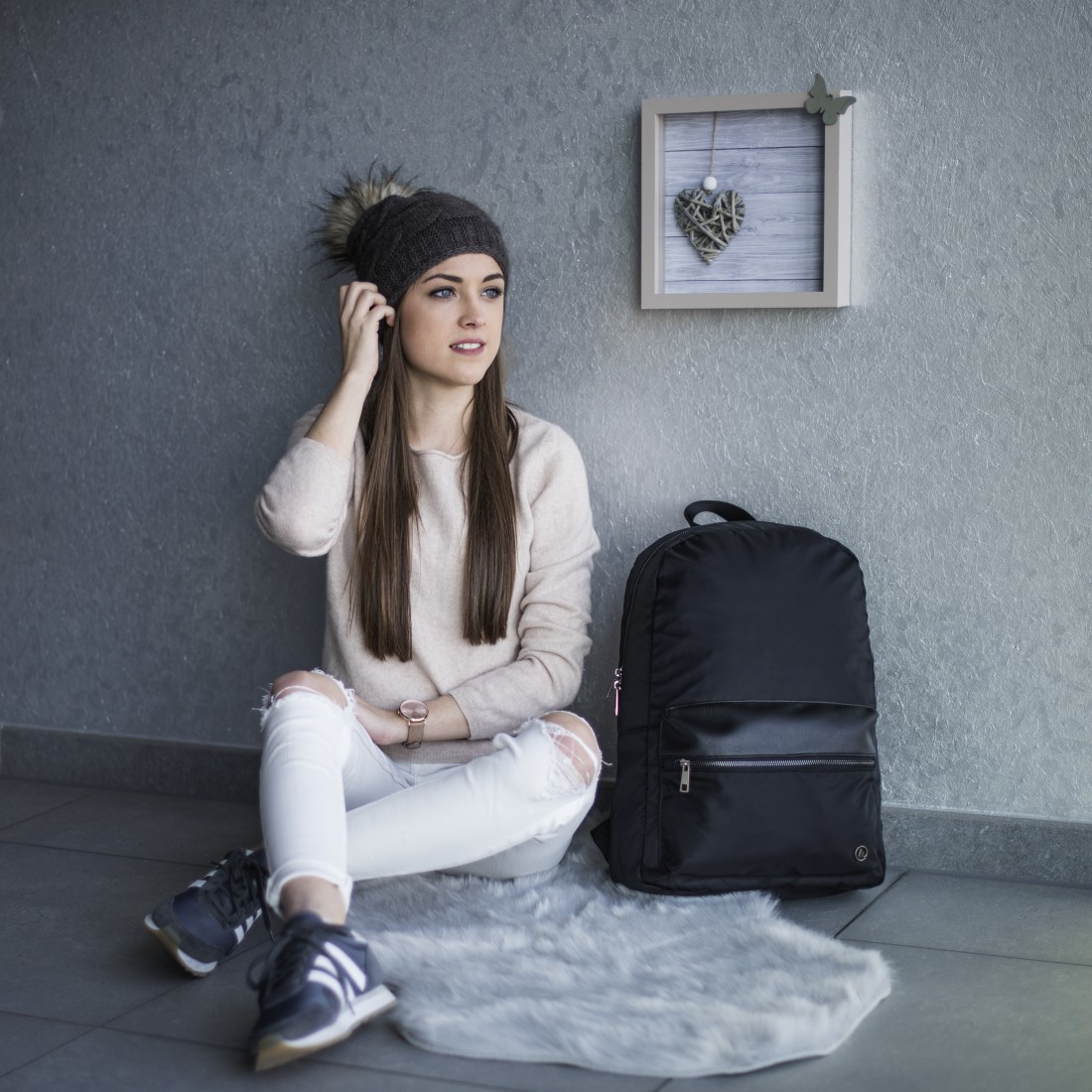 Eine Frau sitzt, fasst sich an den Kopf, trägt einen Hut, in der Nähe eines Rucksacks und eines Teppichs.