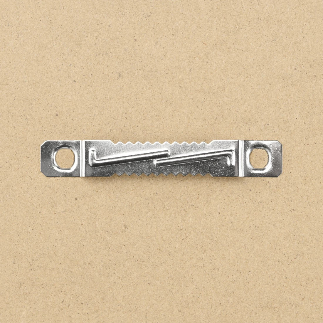 Metalowy wieszak do obrazów w kształcie zęba piły na jasnobrązowej powierzchni.