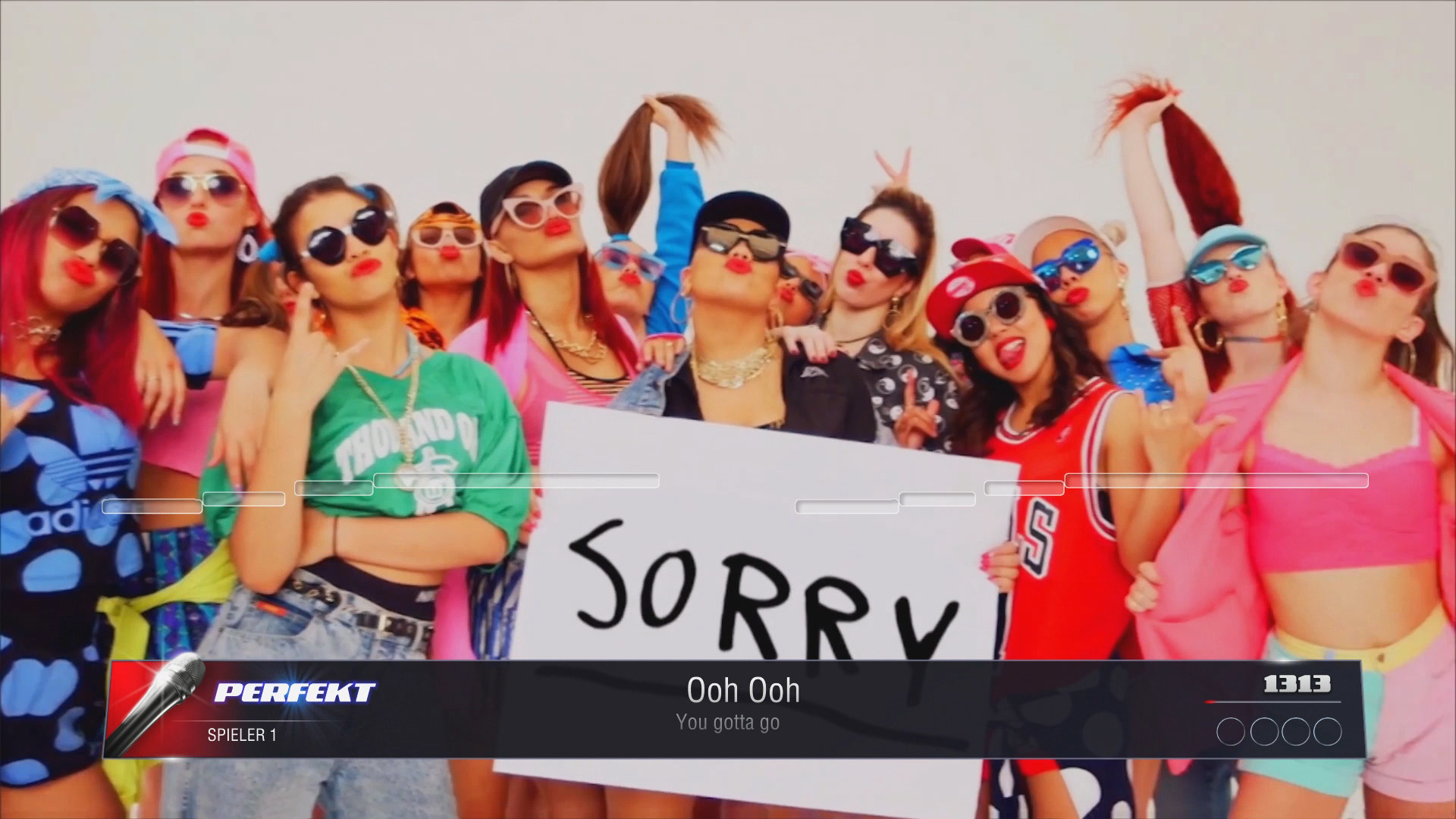 Eine Gruppe von Frauen in Sonnenbrillen und bunten Outfits. Sie halten ein Schild mit 'SORRY'.