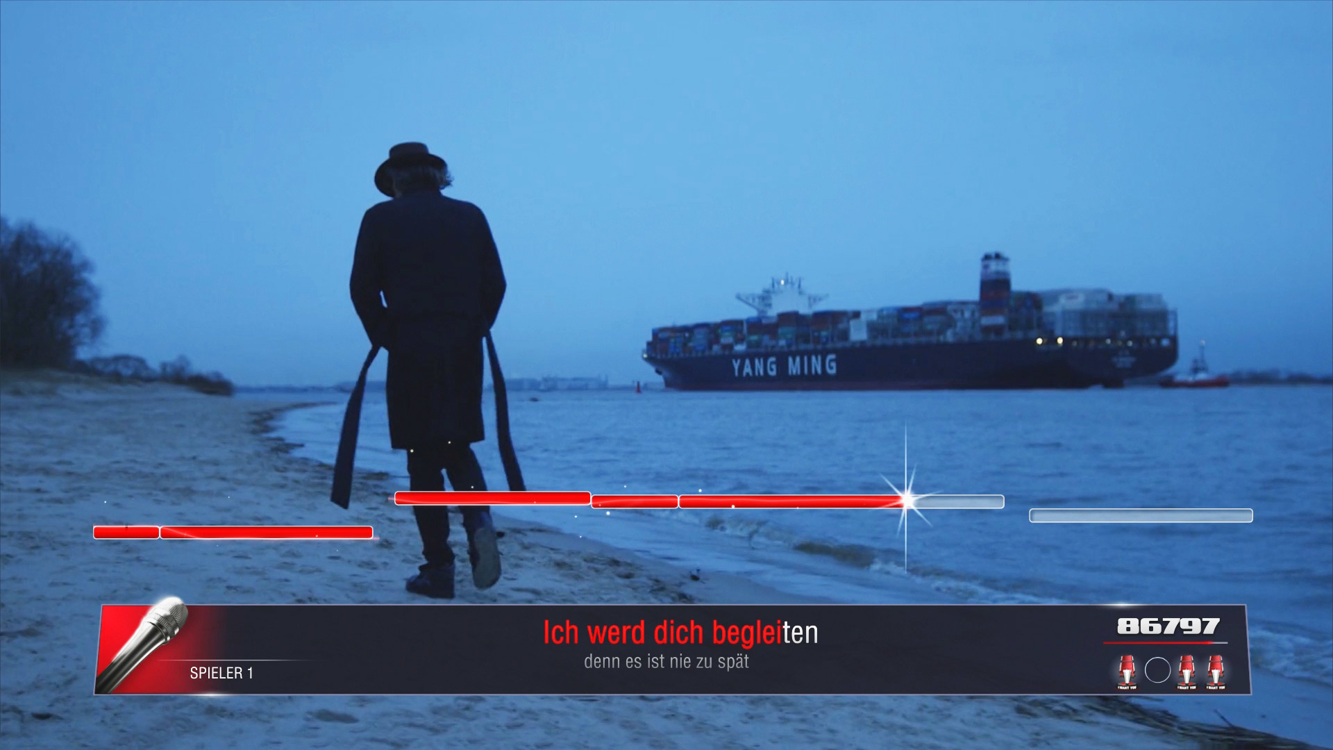 Eine Person geht am Strand, ein Schiff und Küstenlinie in der Ferne.