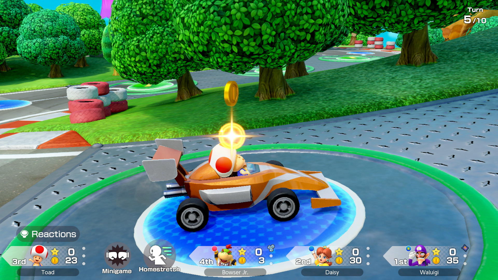 Scena z Mario Kart. Toad jedzie pomarańczowym gokartem po torze. Widoczne są inne postacie, z tablicą wyników w rogu.