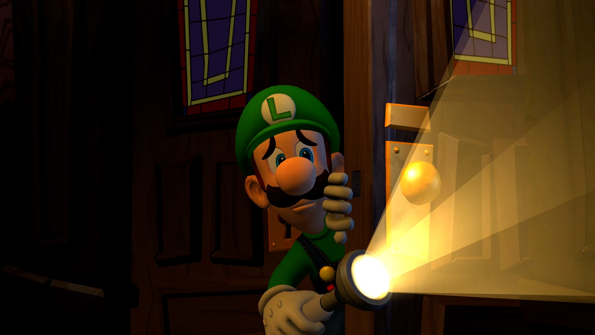Luigi tenant une lampe de poche dans une pièce sombre. Une porte est en arrière-plan.