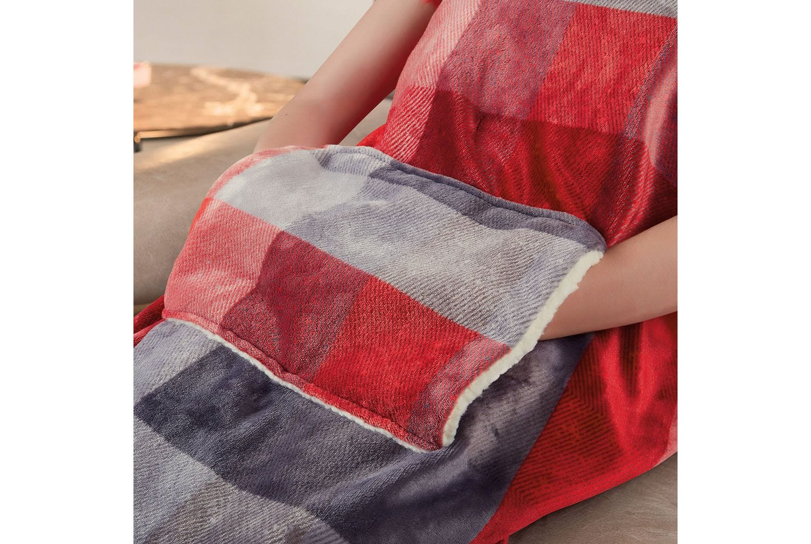 Persona con coperta a quadri rossi e grigi con tasche per le mani. Sfondo beige.