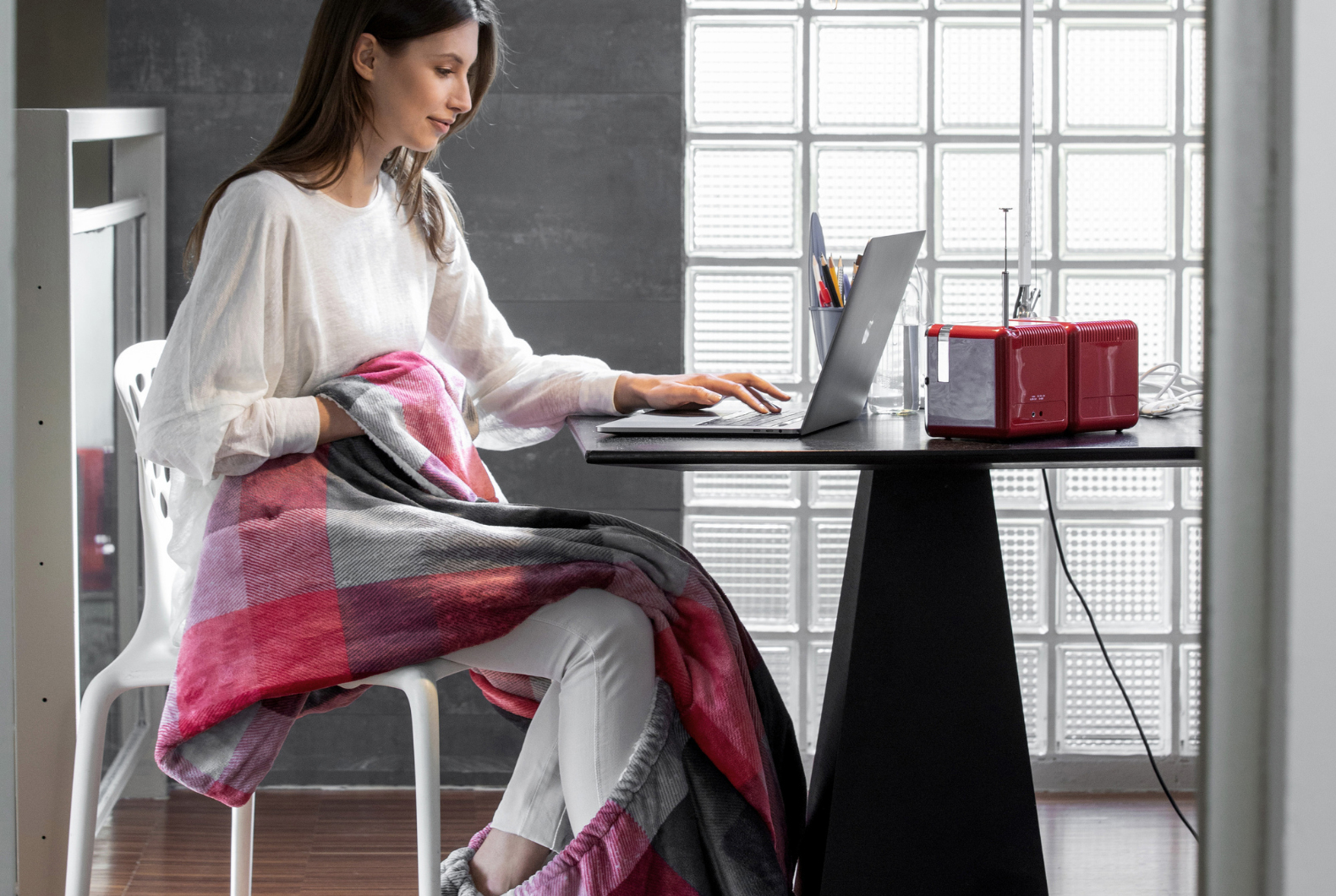 Donna che lavora su un laptop, avvolta in una coperta a quadri rossa e grigia.