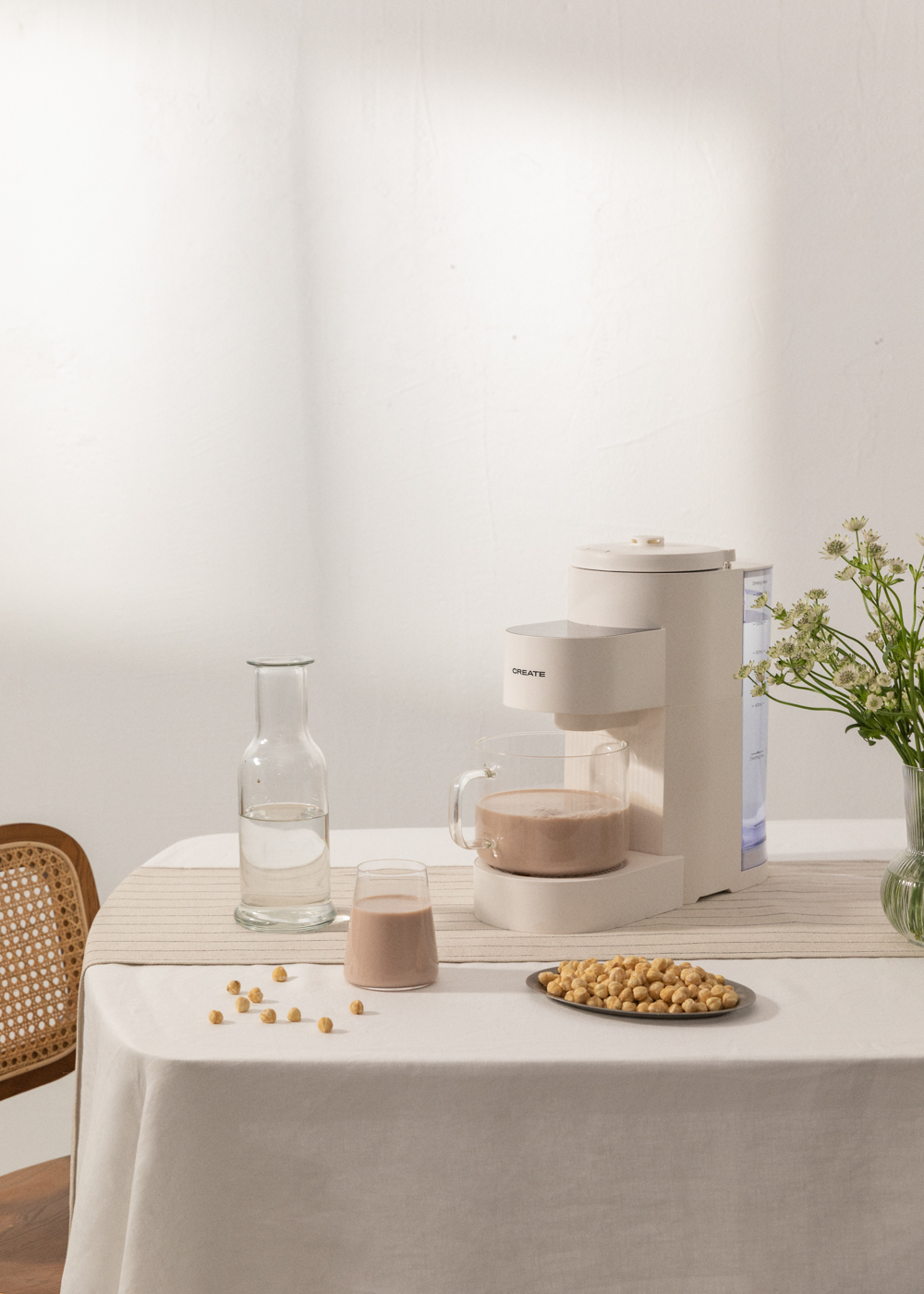 Una máquina blanca con una taza de bebida e ingredientes sobre una mesa con flores.