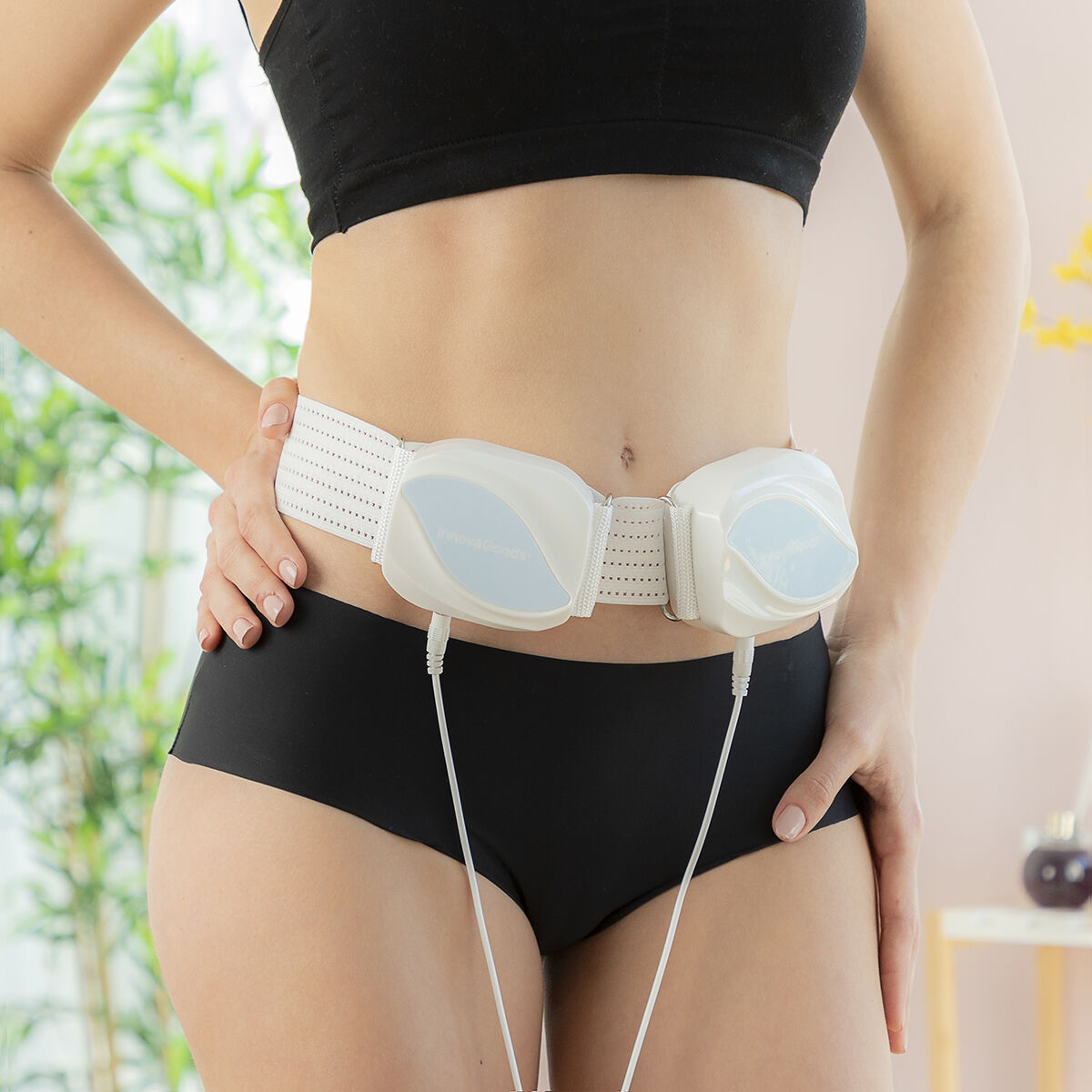 Mujer con un cinturón estimulador muscular electrónico blanco enrollado alrededor de su cintura, con las manos en las caderas.