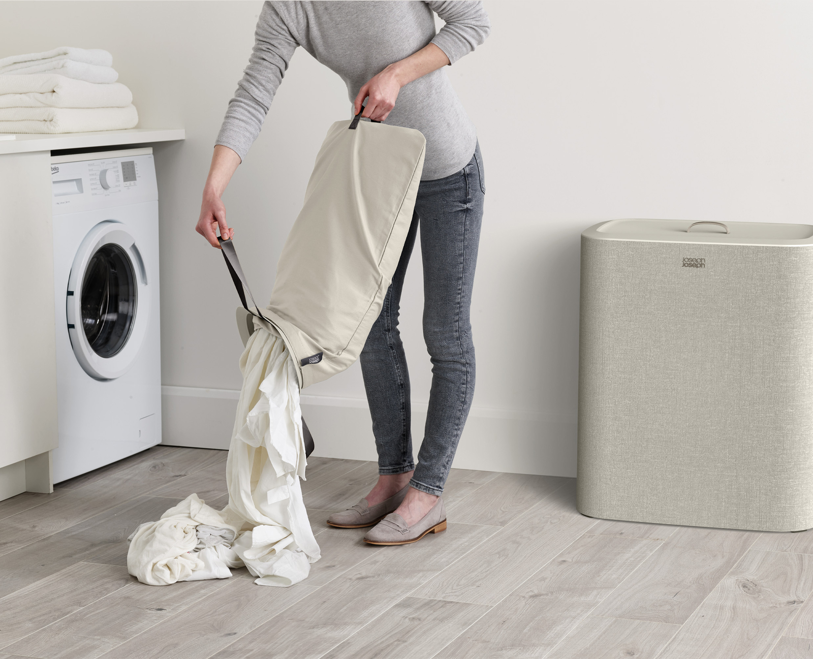 Eine Person leert einen Wäschebeutel voller weißer Kleidung auf den Boden, neben einem Wäschekorb.