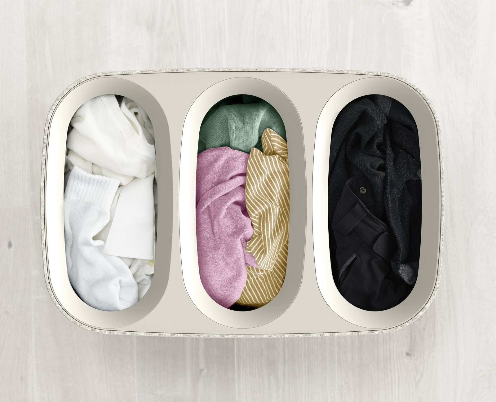 Wäschekorb mit drei Fächern, gefüllt mit weißer, rosa gestreifter und schwarzer Kleidung, Draufsicht.