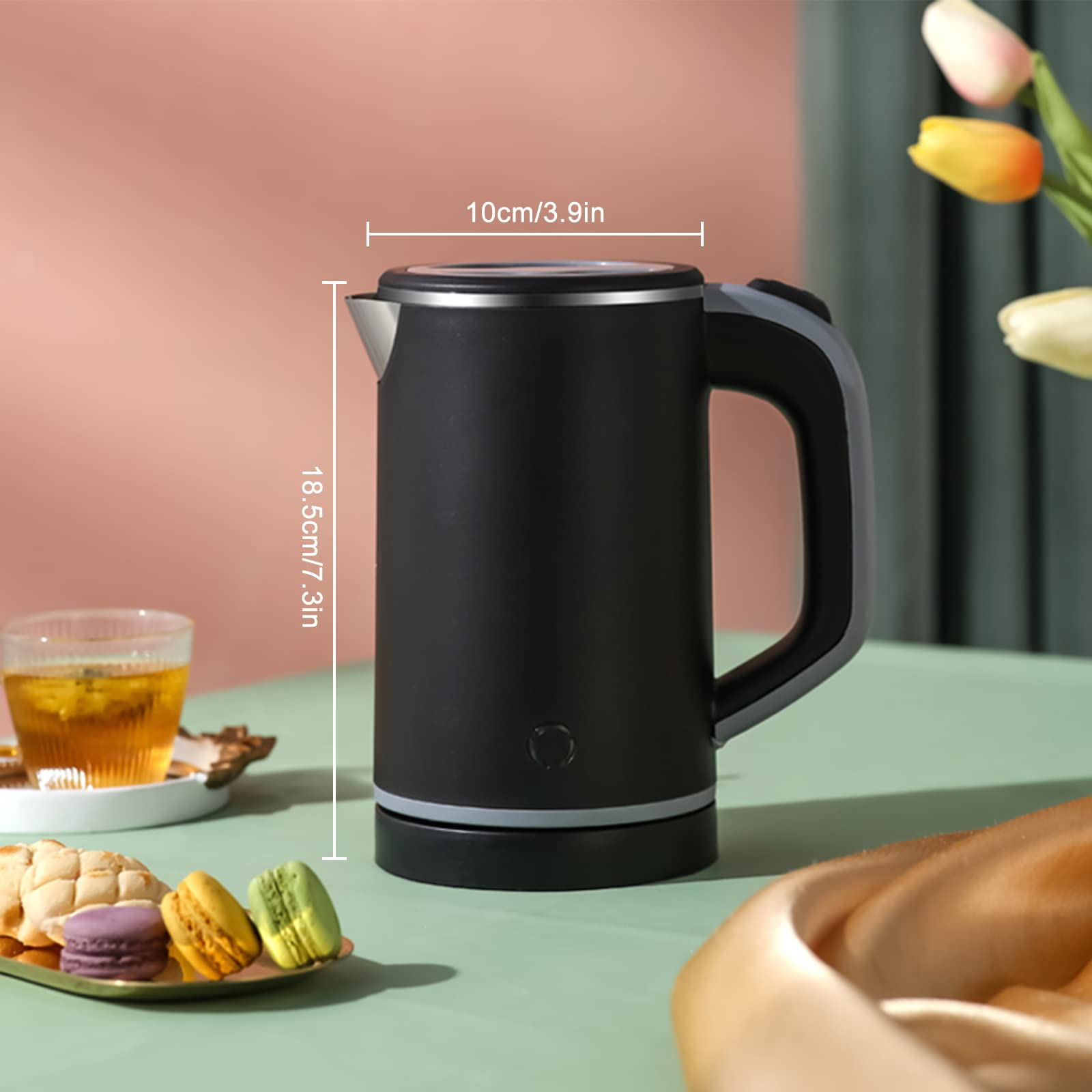 Schwarzer Wasserkocher mit Abmessungen, auf einem Tisch mit Makronen und Tee, Hintergrundblumen.