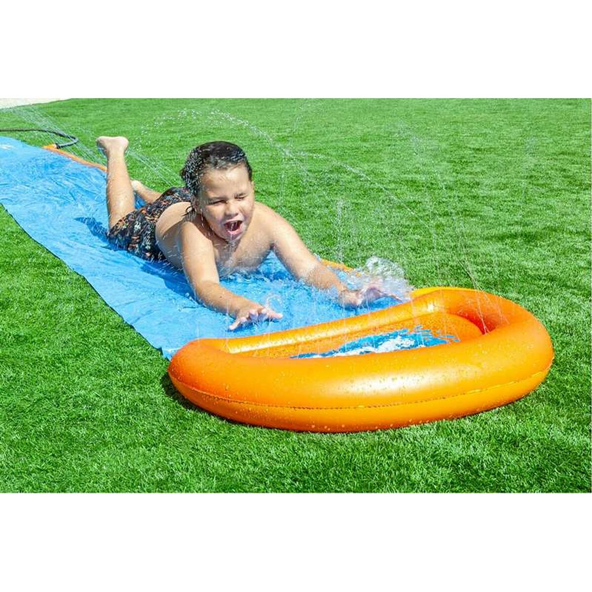 Ein kleiner Junge, der auf einer blauen Wasserrutsche rutscht. Am Ende befindet sich ein orangener Stoßfänger.