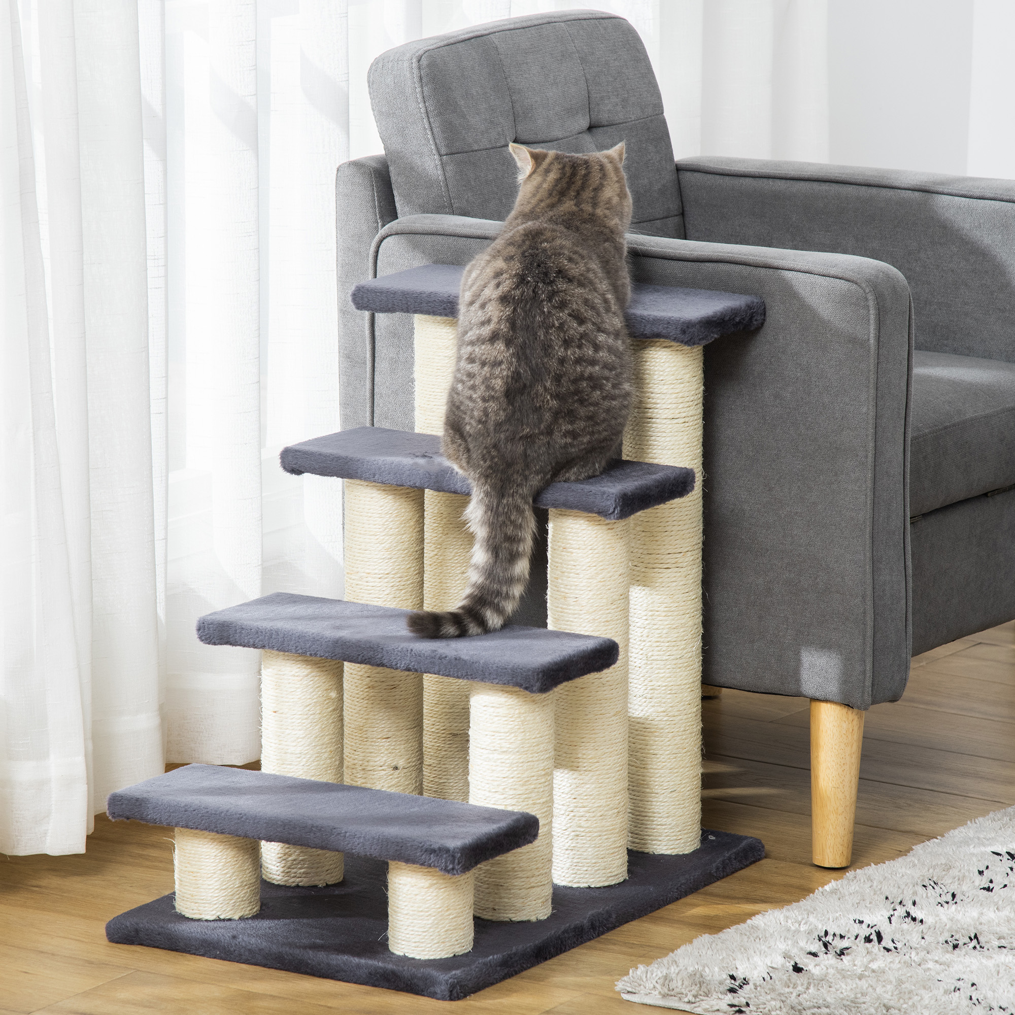 Eine Katze klettert auf einem Kratzbaum, im Hintergrund ein graues Sofa.