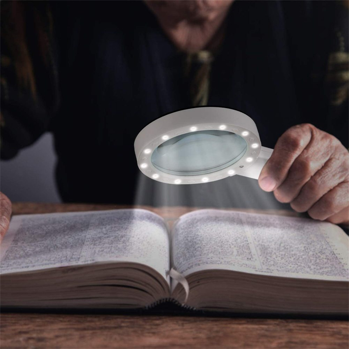 Person benutzt eine weiße Lupe mit Licht, um ein Buch zu lesen.