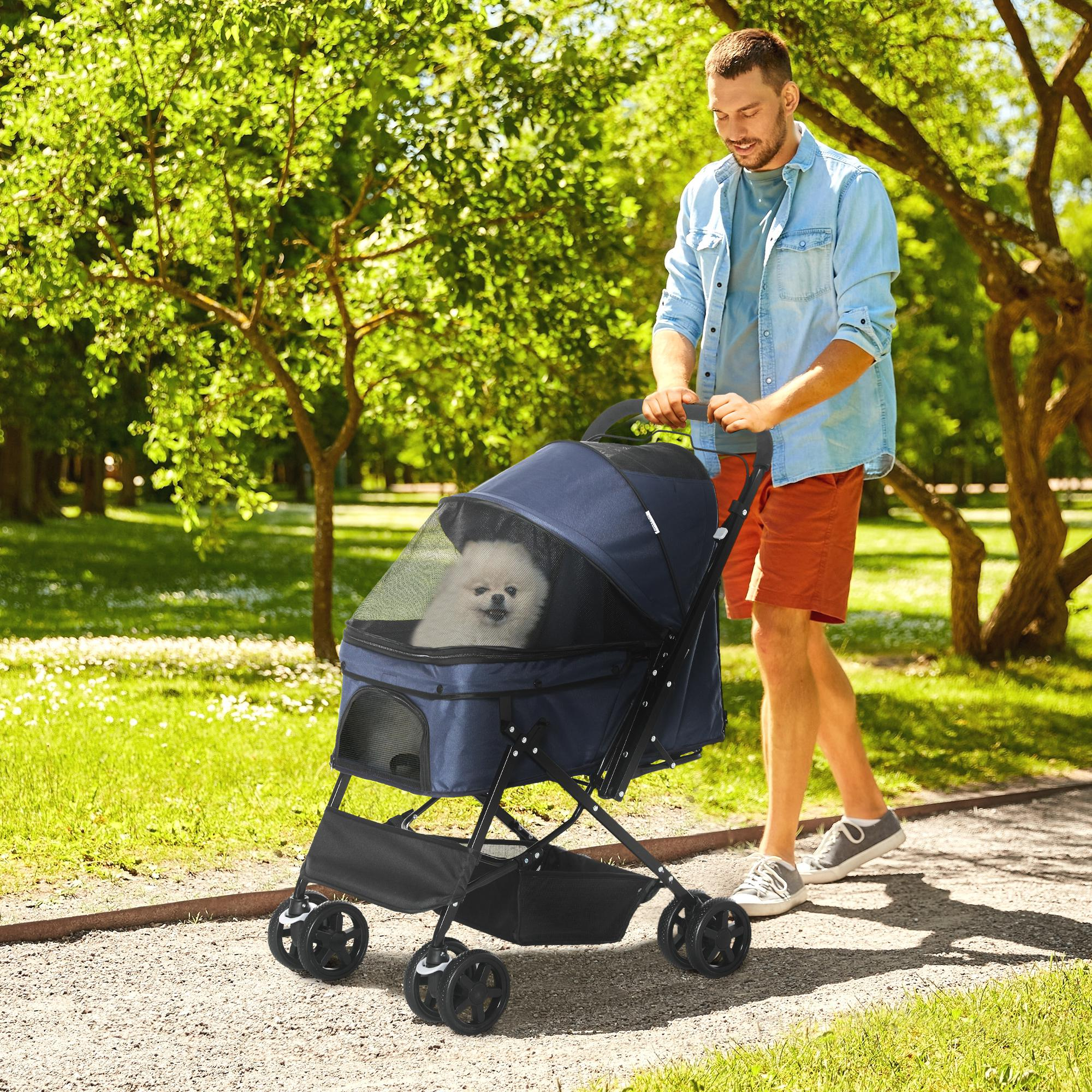 Mann schiebt einen blauen Haustier-Kinderwagen mit Hund darin in einem Park.