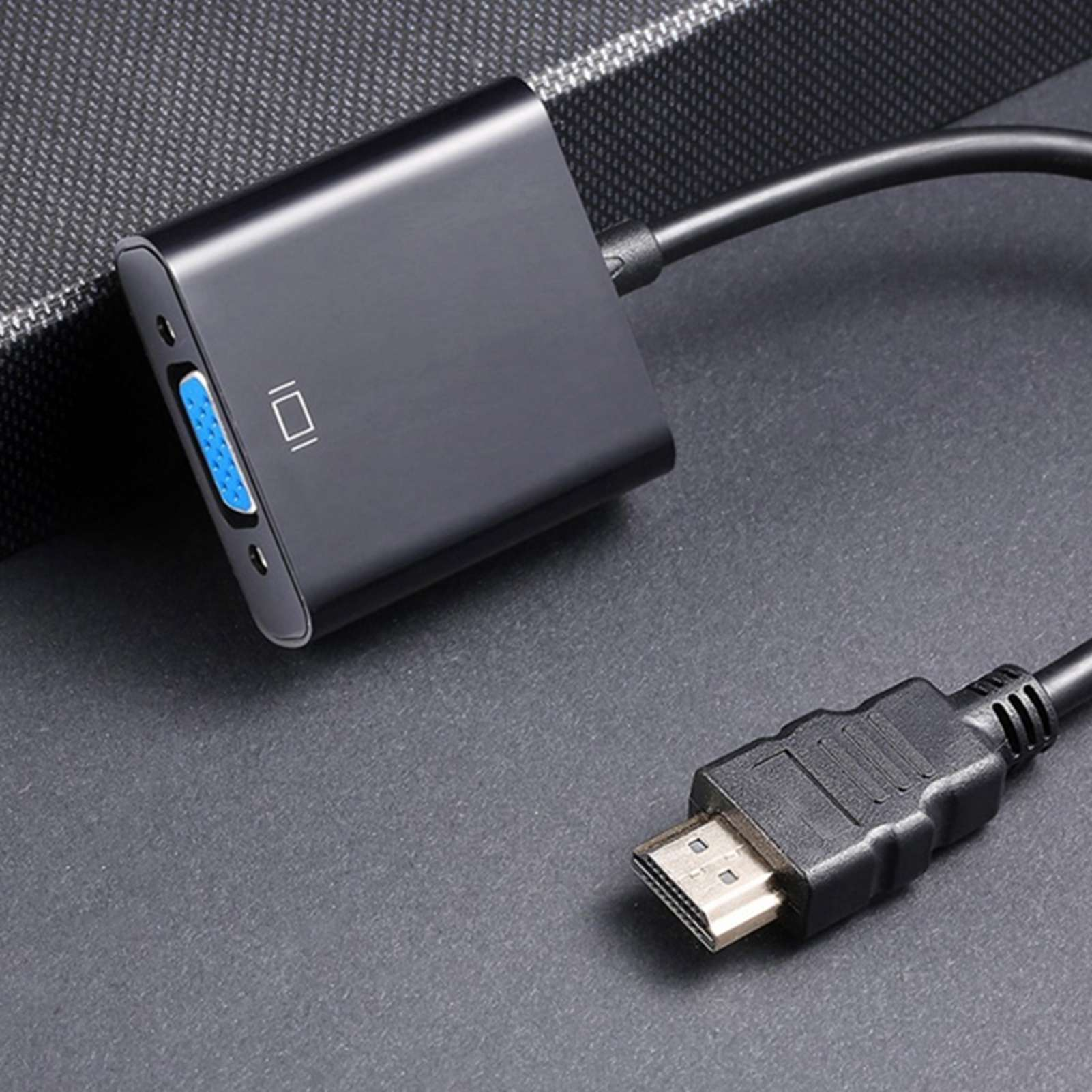 Schwarzer HDMI-zu-VGA-Adapter mit schwarzem Kabel auf grauer Oberfläche.