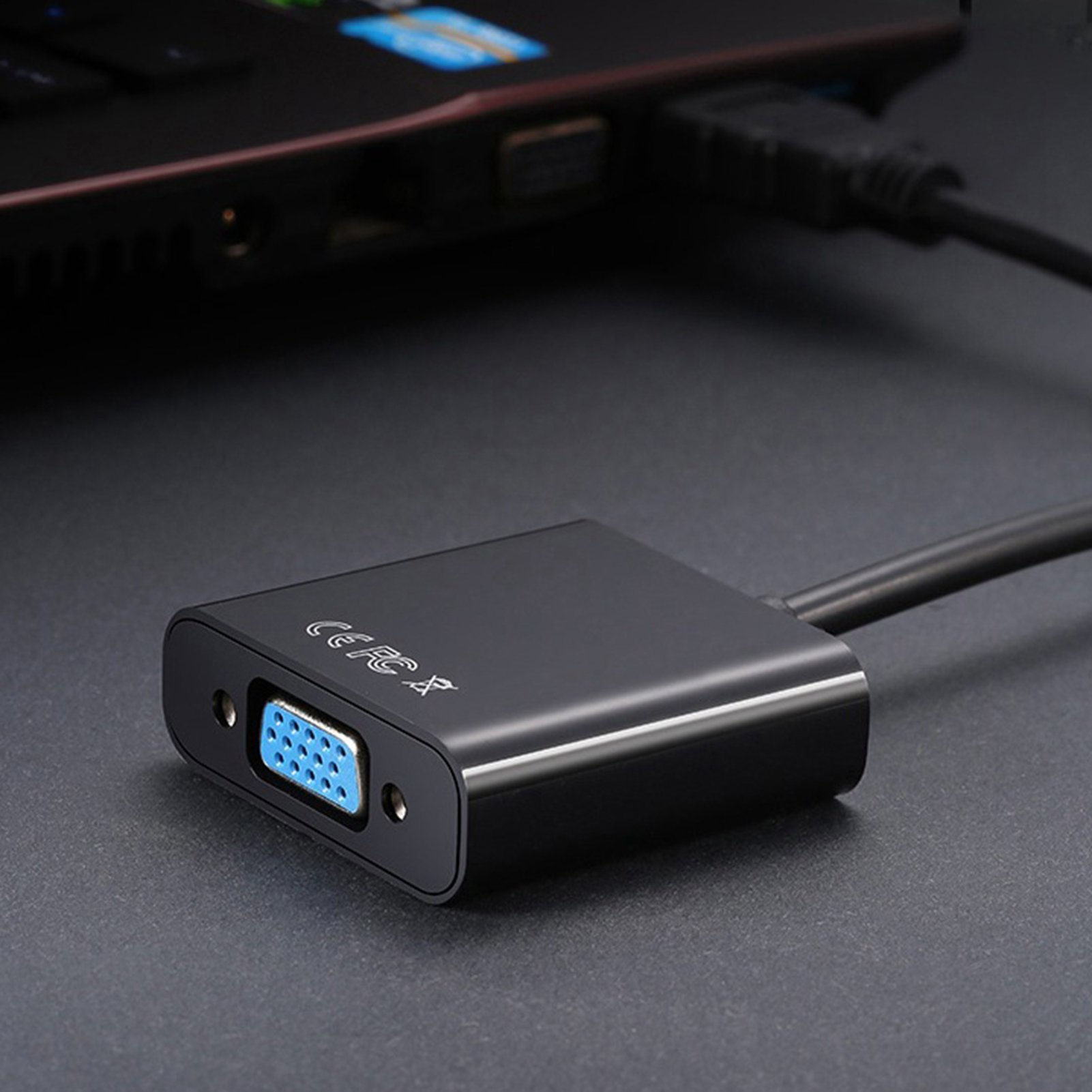 Schwarzer HDMI-zu-VGA-Adapter, der an einen Laptop angeschlossen ist. VGA-Anschluss ist sichtbar.